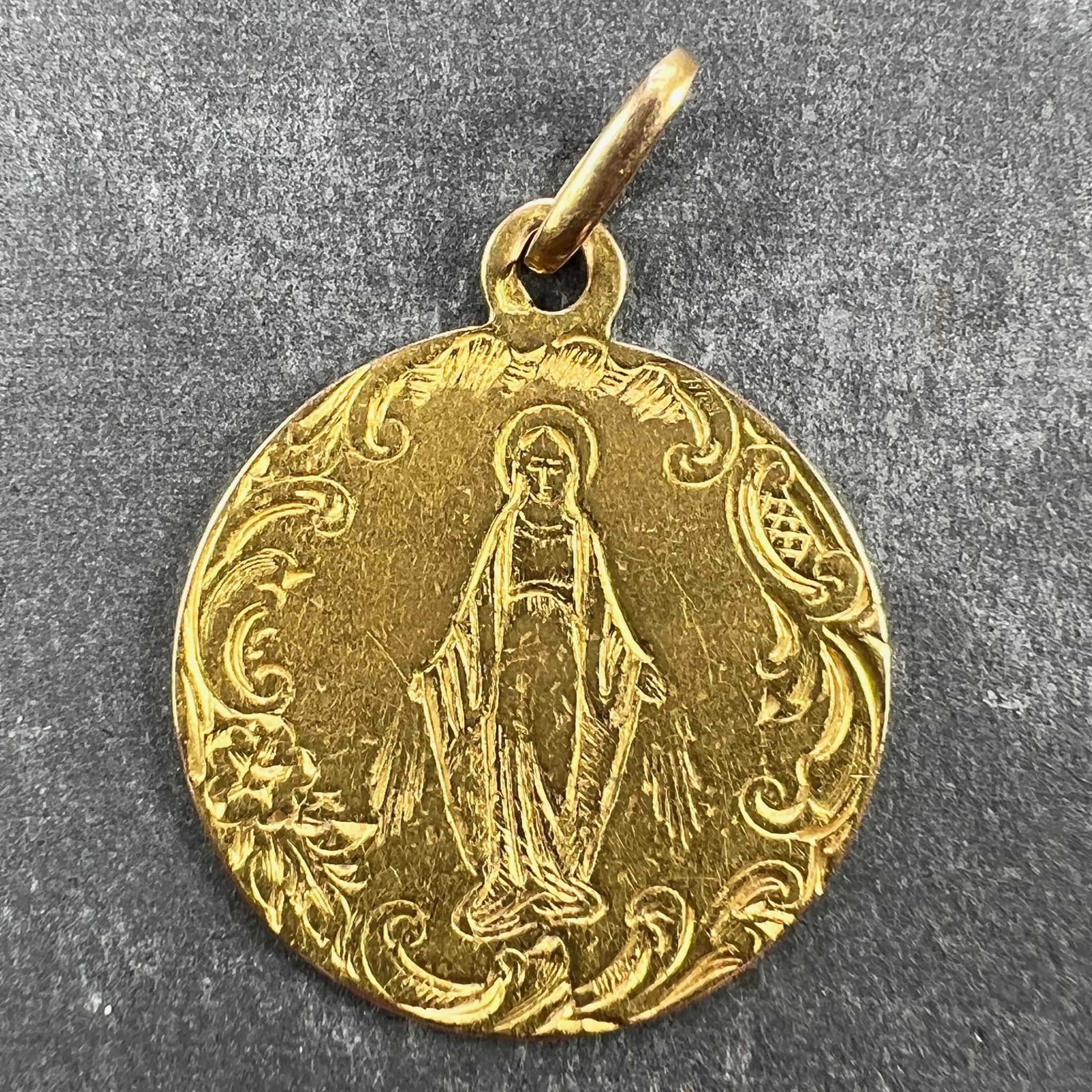 A French 18 karat (18K) yellow gold charm pendant designed as a round medal engraved with the Virgin Mary within an engraved scrolled border. Stamped with the eagle's head for 18 karat gold and French manufacture.

Dimensions: 2.1 x 1.8 x 0.06 cm