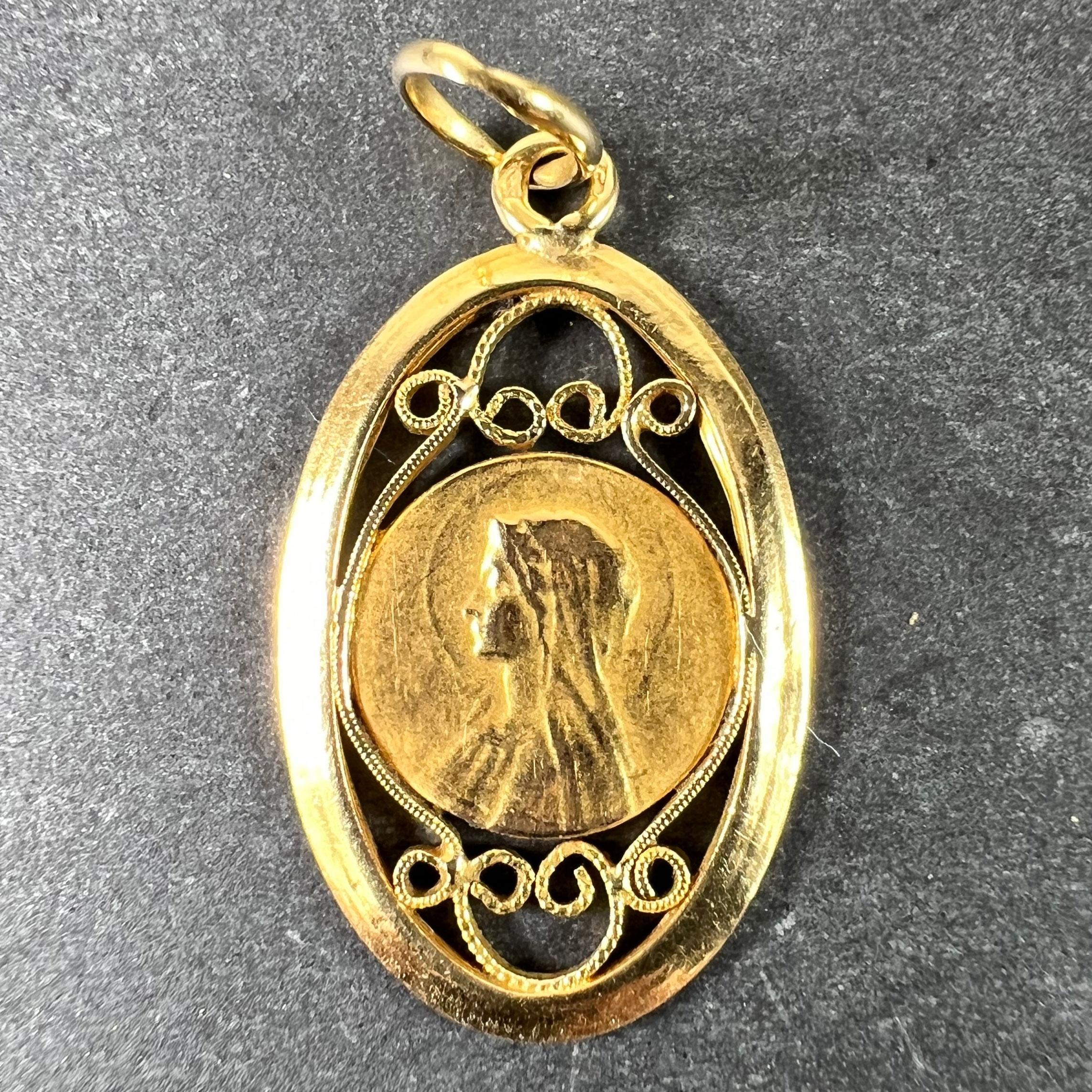 A French 18 karat (18K) yellow gold charm pendant designed as a round medal depicting the Virgin Mary within a navette shaped frame with curliques of filigree gold wire. Stamped with the eagle's head mark for 18 karat gold and French manufacture