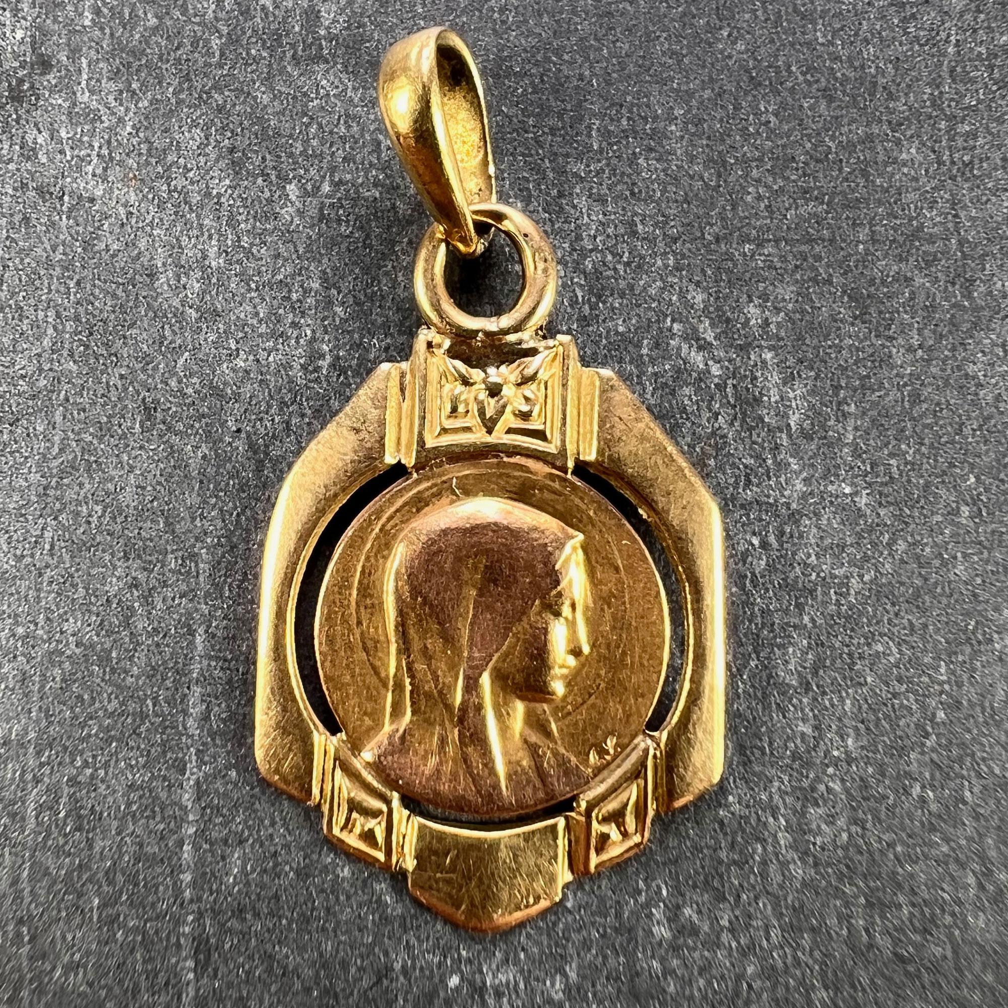 A French 18 karat (18K) yellow gold charm pendant designed as a medal depicting the Virgin Mary signed AS within a yellow gold frame with geometric stripes of heart and floral decoration. The reverse of the medal depicts Jesus Christ emerging from