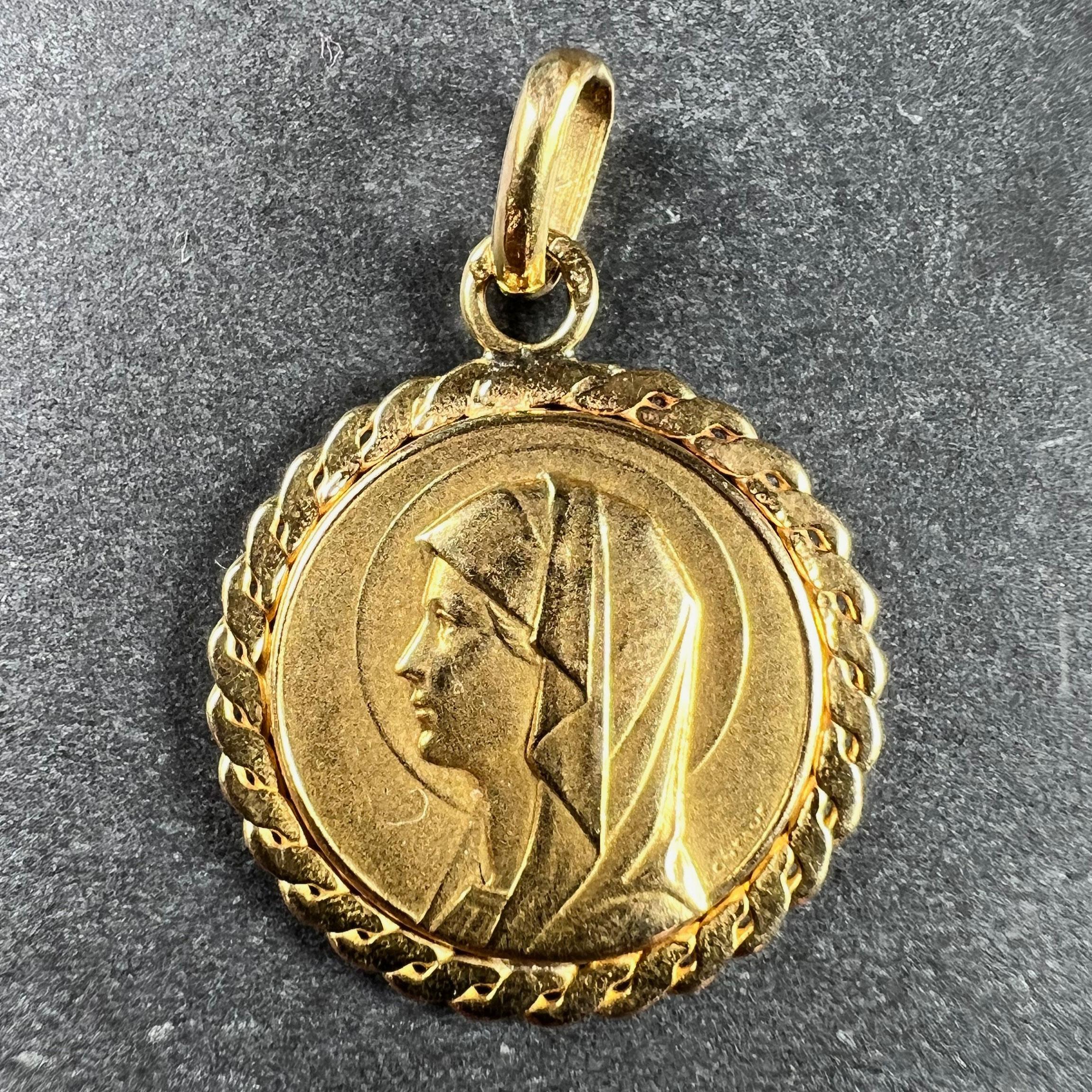 A French 18 karat (18K) yellow gold charm pendant designed as a medal depicting the Virgin Mary within a twisted frame. The reverse depicts a woman praying outside a grotto in which the Virgin Mary stands surrounded by roses and lilies. Stamped with
