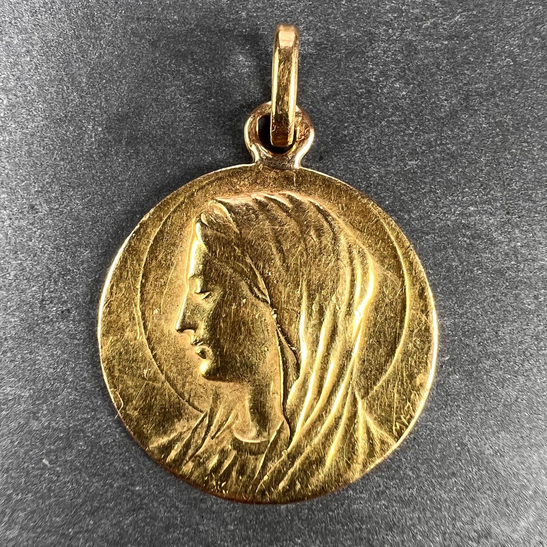 A French 18 karat (18K) yellow gold charm pendant designed as a medal depicting the Virgin Mary. Signed Mazzoni. Stamped with the horse’s head  mark for 18 karat gold and French manufacture between 1838-1919. The reverse depicting a lily and