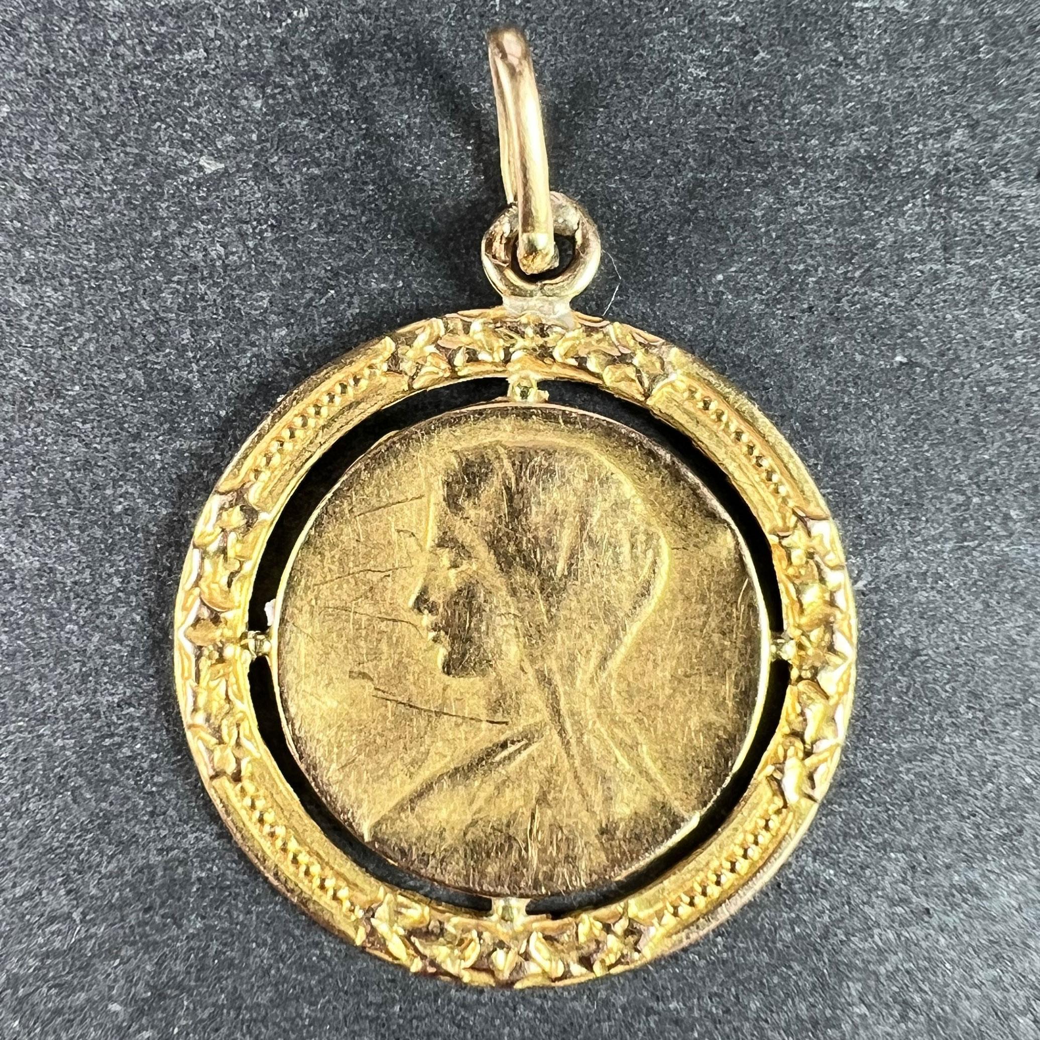 A French 18 karat (18K) yellow gold charm pendant designed as a round medal depicting the Virgin Mary within a pierced frame of ivy leaves representing eternal love. Stamped with the eagle's head for French manufacture and 18 karat gold, and a