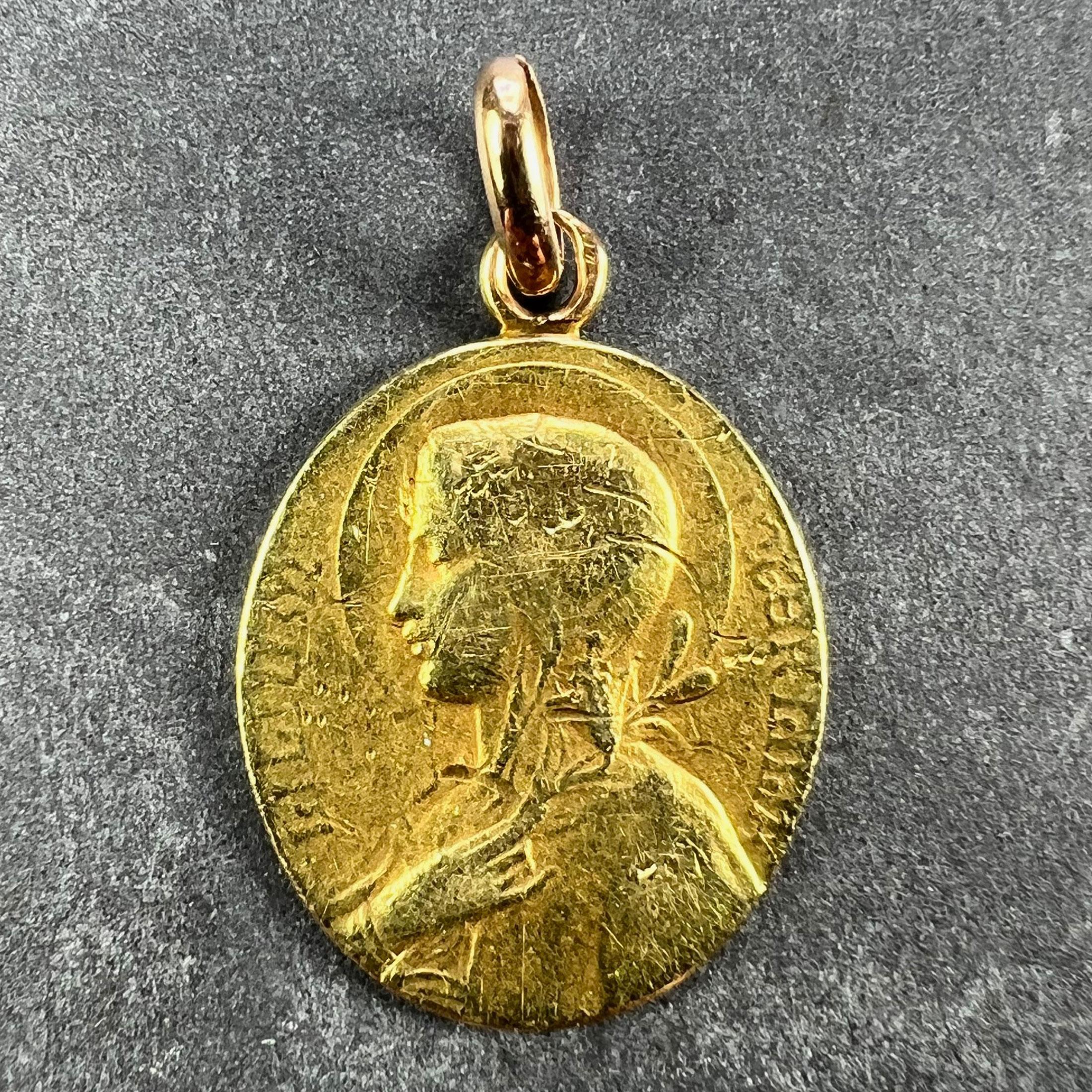 A French 18 karat (18K) yellow gold charm pendant designed as an oval medal representing the Virgin Mary with a lily to one side with the phrase 'Lilum inter'Lilia' (Lily among Lilies) surrounding. To the reverse the holy communion bread and wine on