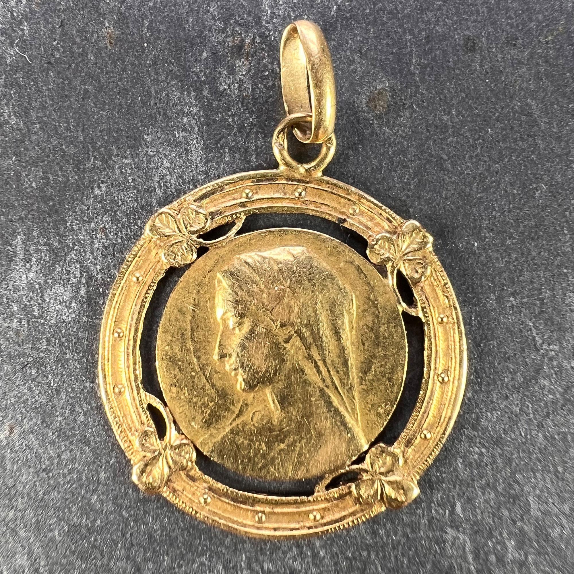 A French 18 karat (18K) yellow gold charm pendant designed as a round medal depicting the Virgin Mary within a pierced frame of lucky clover leaves. The leaves also engraved to the reverse. Stamped with the eagle's head for French manufacture and 18