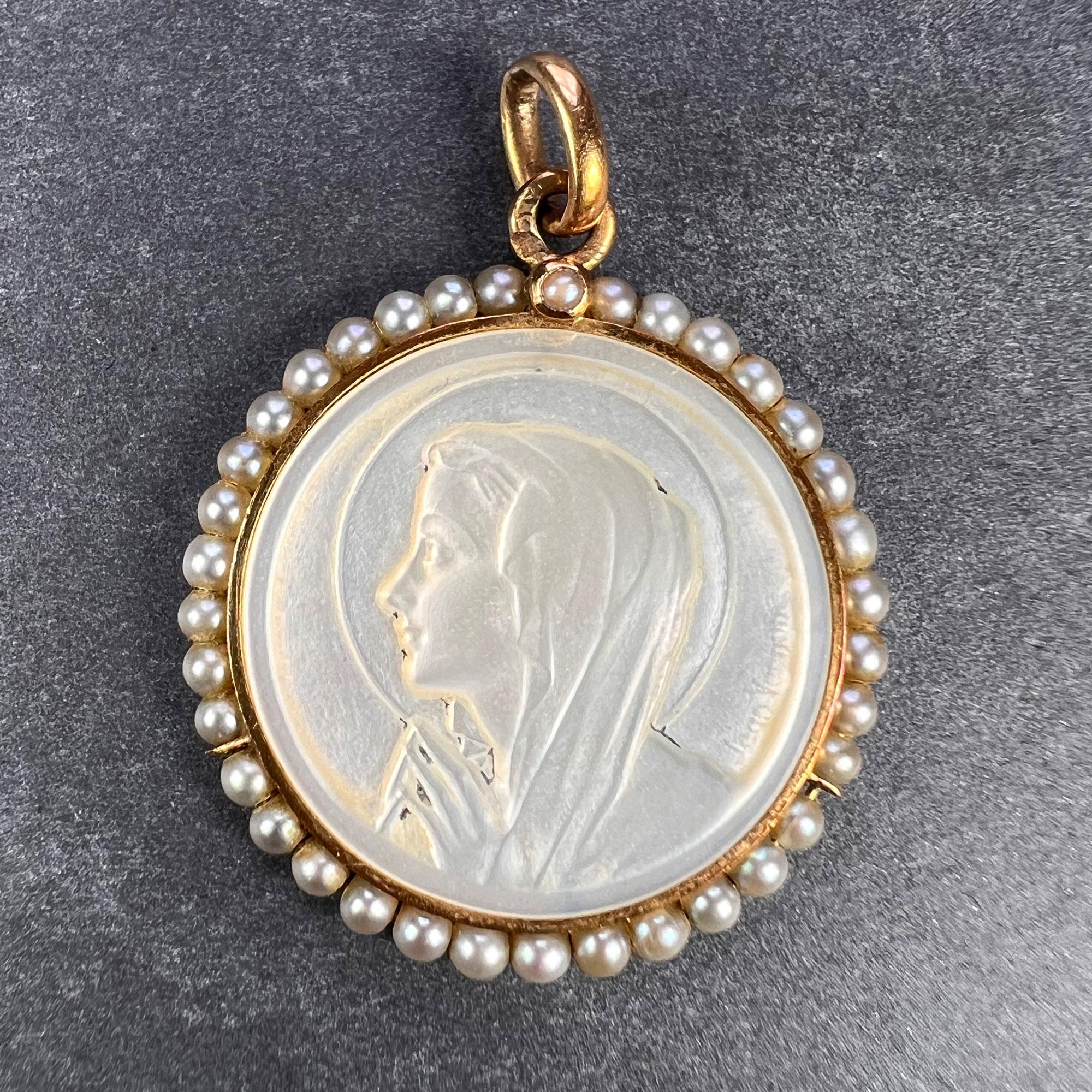 A French 18 karat (18K) yellow gold charm pendant designed as a mother-of-pearl medal depicting the Virgin Mary carved and signed by Jean Vernon surrounded by 36 natural seed pearls. Stamped with the eagle mark for 18 karat gold and French