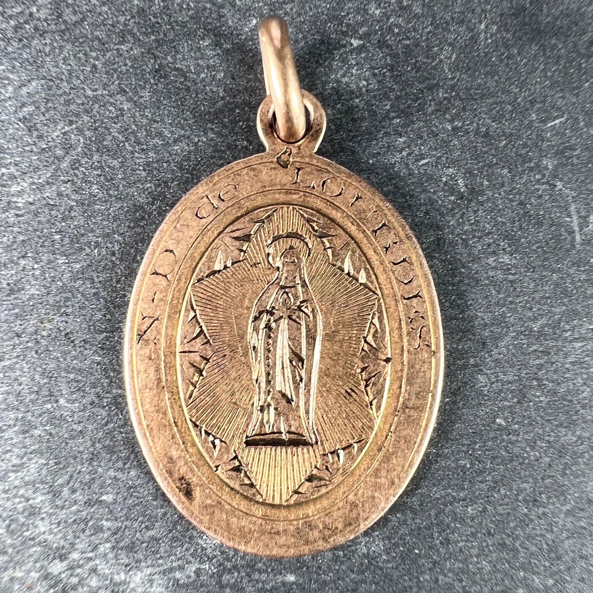 A French 18 karat (18K) rose gold charm pendant designed as an oval medal depicting the Virgin Mary within a frame engraved N-D de Lourdes for Notre Dame de Lourdes. Stamped with the horse's head for 18 karat gold and French (Lourdes) manufacture