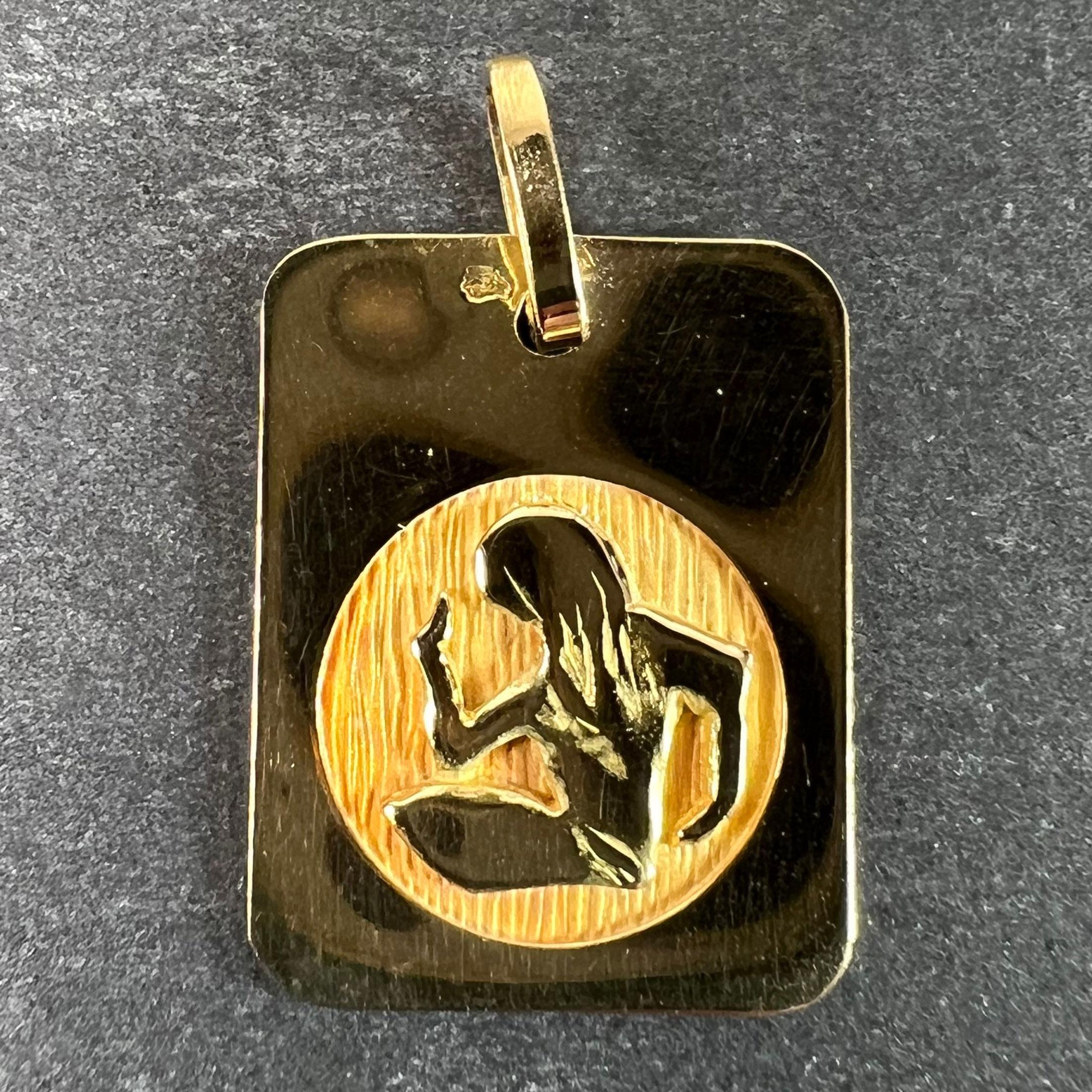 A French 18 karat (18K) yellow gold charm pendant designed as a rectangular medal with an engraved circular recess depicting a woman dressing her hair representing the zodiac star sign of Virgo. Stamped with the eagle’s head for French manufacture