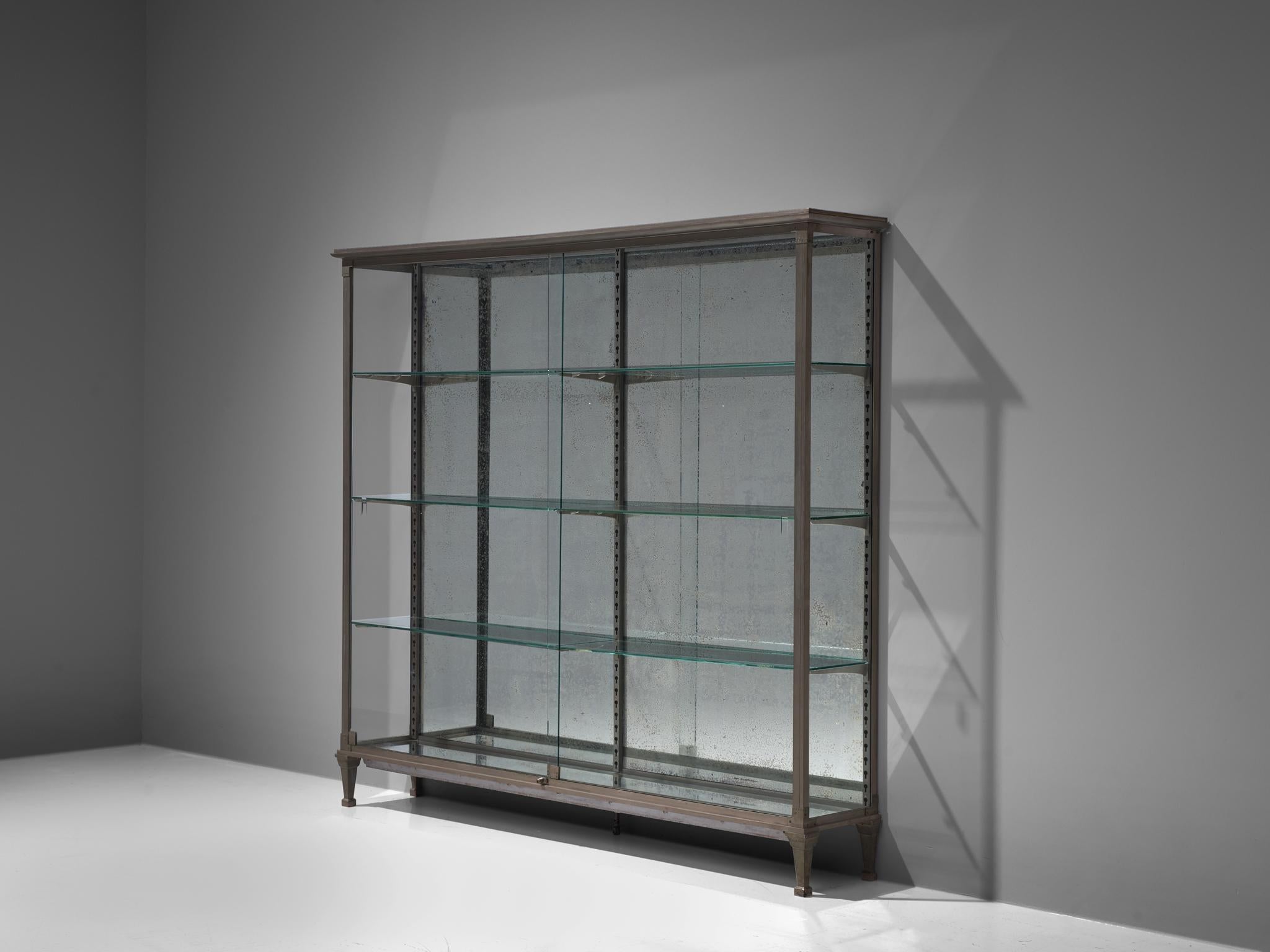 Large vitrine, glass, metal, mirrored glass, France, 1950s

Elegant glass vitrine with mirrored glass in the back and bottom which shows an admirable patina. Through the glass slidings doors in the front you have access to the interior. The glass