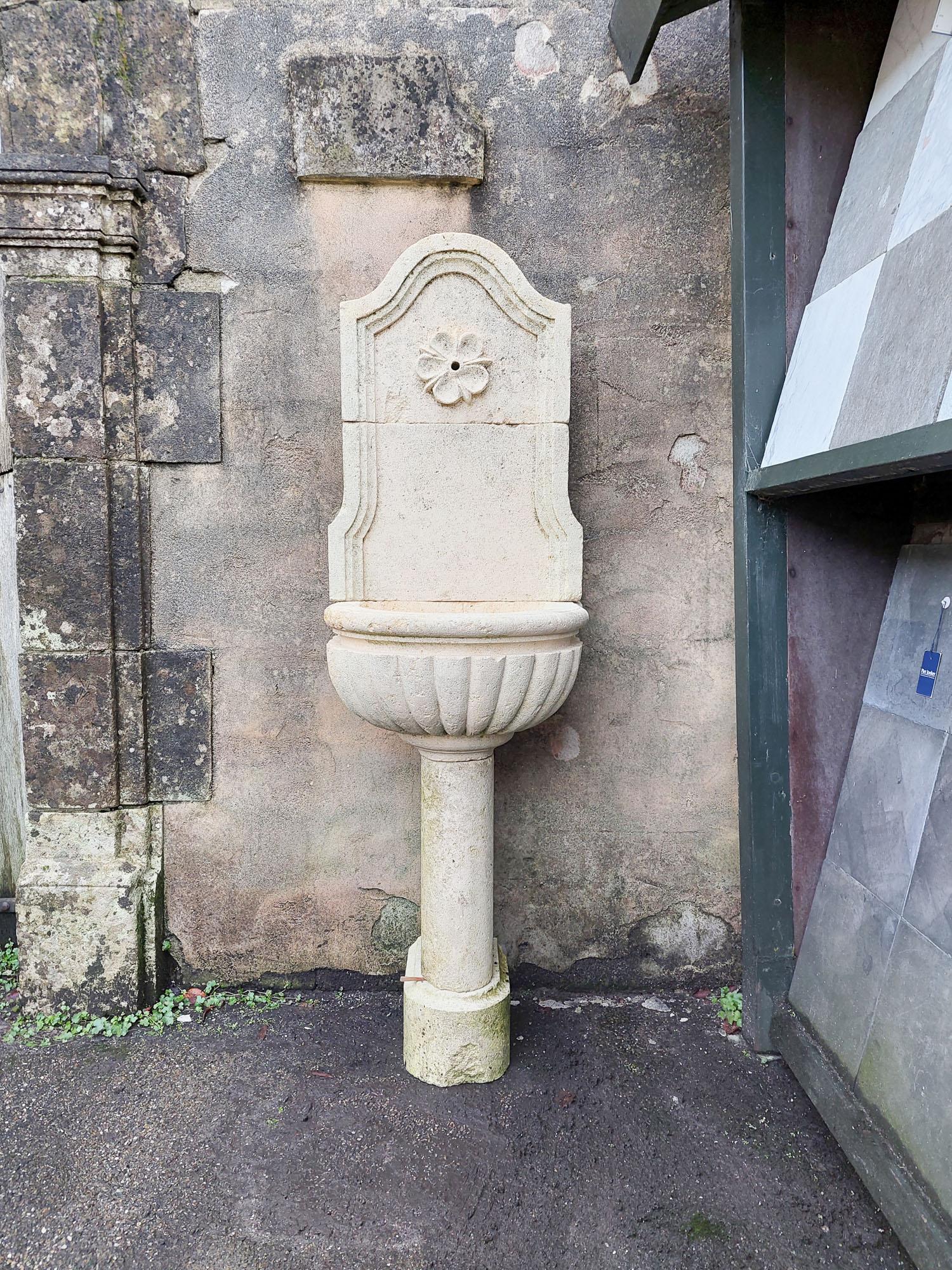 French wall fountain made of light limestone, the bowl with a lobed edge and a flower / rosette around the tap hole.

h 156 x w 49 x d 50 cm