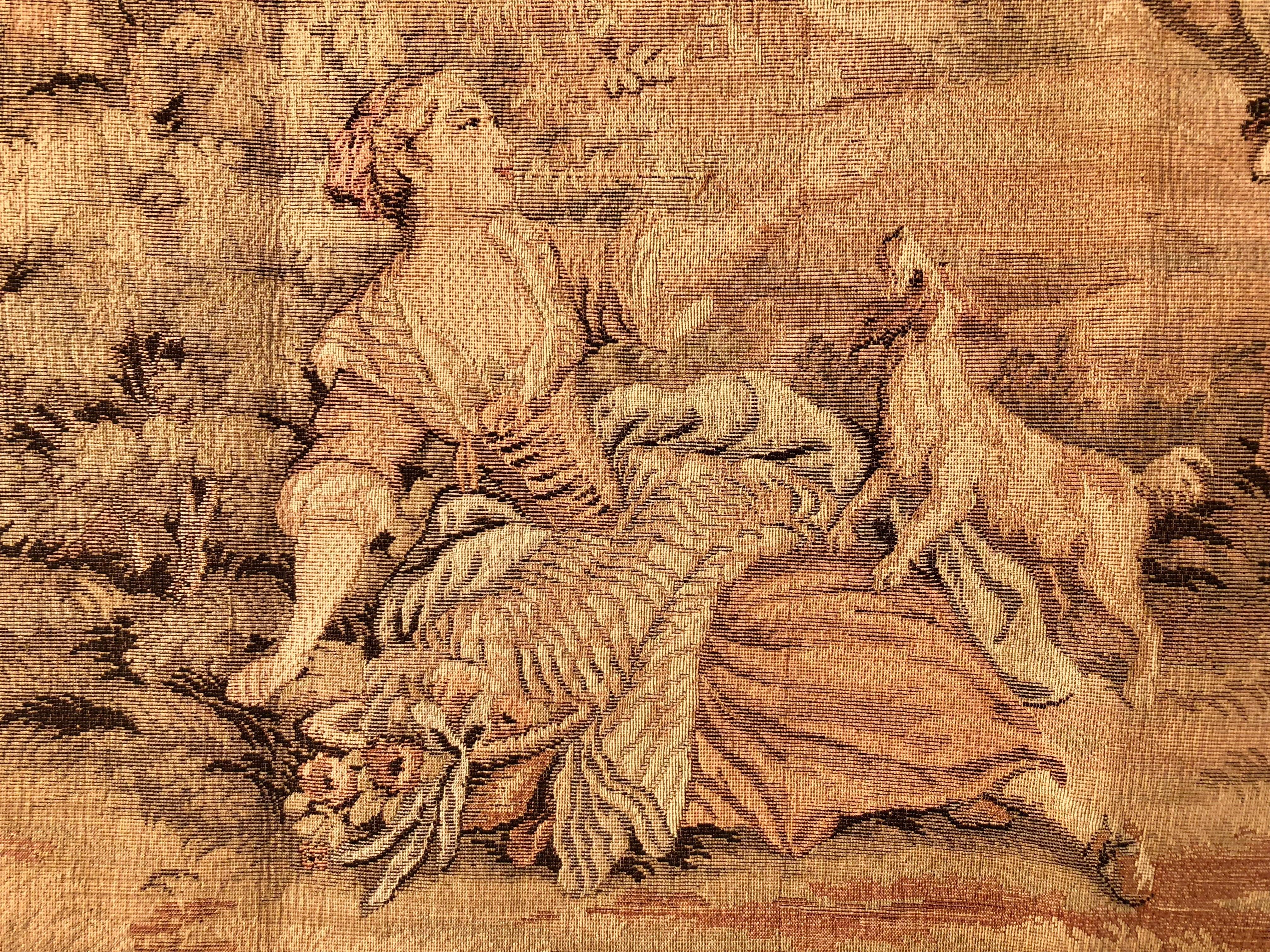 This is a lovely French wall hanging tapestry of a pastoral scene from the 1900s. There is one woman lounging in the yard with her dog while another is on a swing being pushed by a man while a child is sitting on the ground with a dog on his lap.