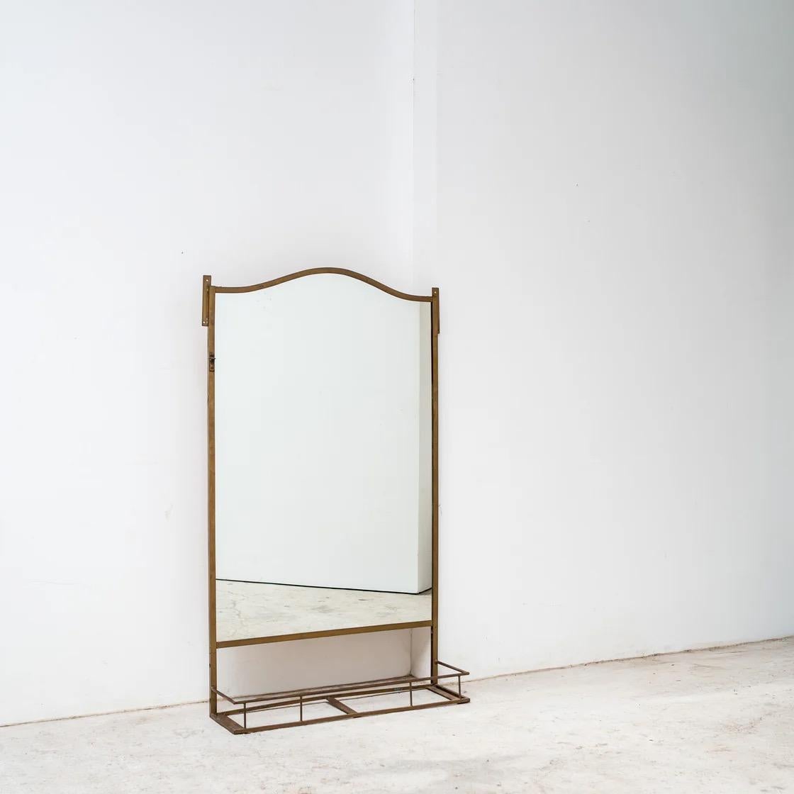 Un grand miroir mural ou sur pied avec un cadre arqué élégant et un plateau inférieur en métal. Sa structure raffinée et sa patine naturelle lui confèrent une présence intemporelle, adaptée aussi bien à une atmosphère résidentielle qu'à celle d'une