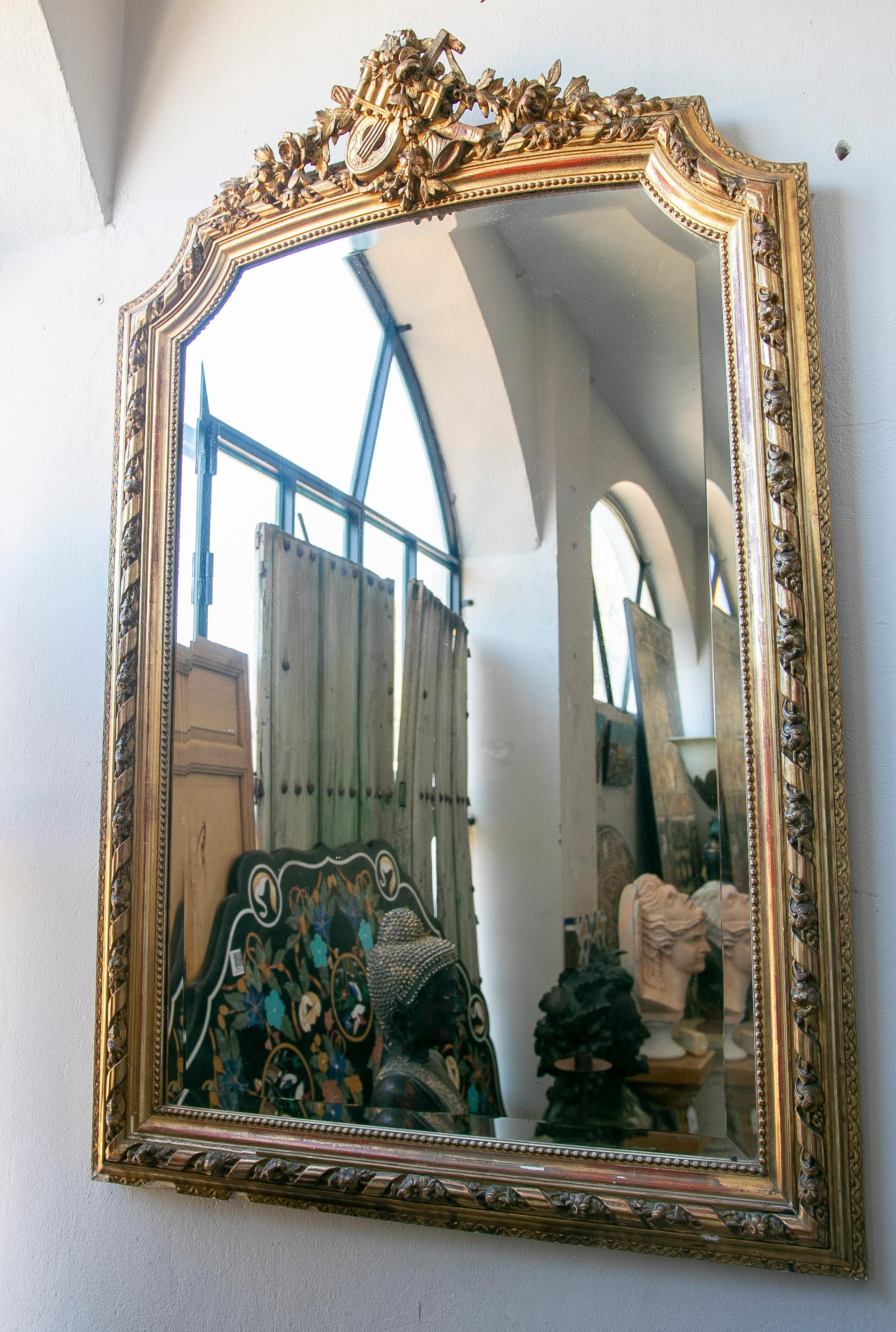 French Wall Mirror in Gilded Wood with  the Coping Decorated with Instruments. Typical of the period.
