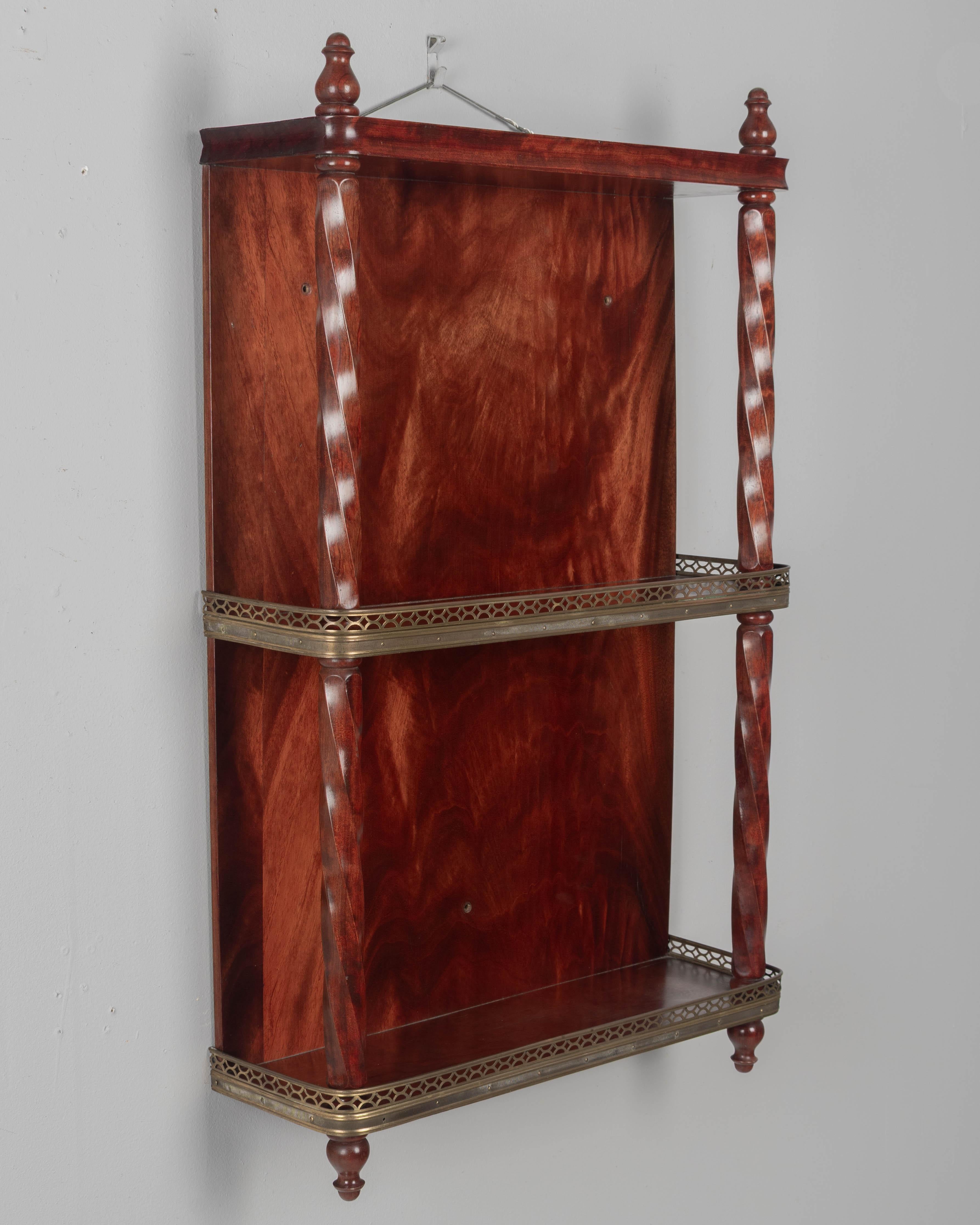 A French wall-mounted mahogany shelf, with turned spindle supports and decorative finials. Two shelves with curved corners and brass gallery. Beautiful flame mahogany veneer back. The back has three holes for mounting to the wall with decorative