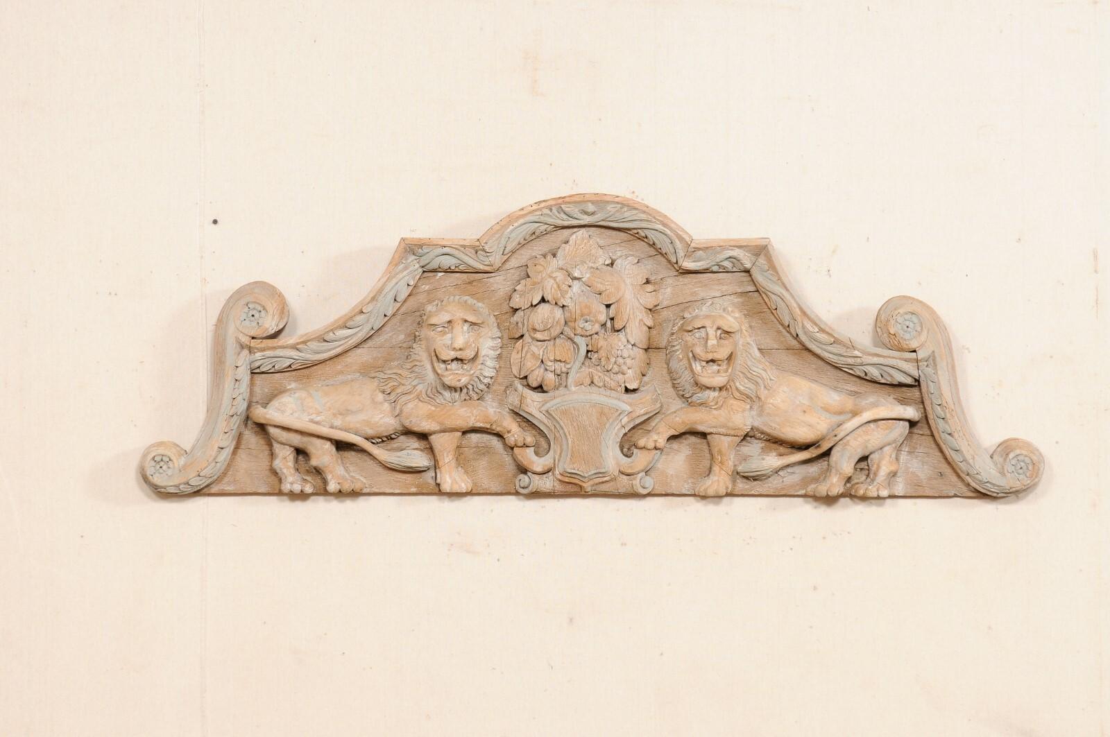 A French architectural carved wood plaque, in a lion motif, from the 19th century. This antique wall decoration from France has a pediment style design with arched top and lovely s-scrolled sides and a flat bottom. There is a heavily carved crest,