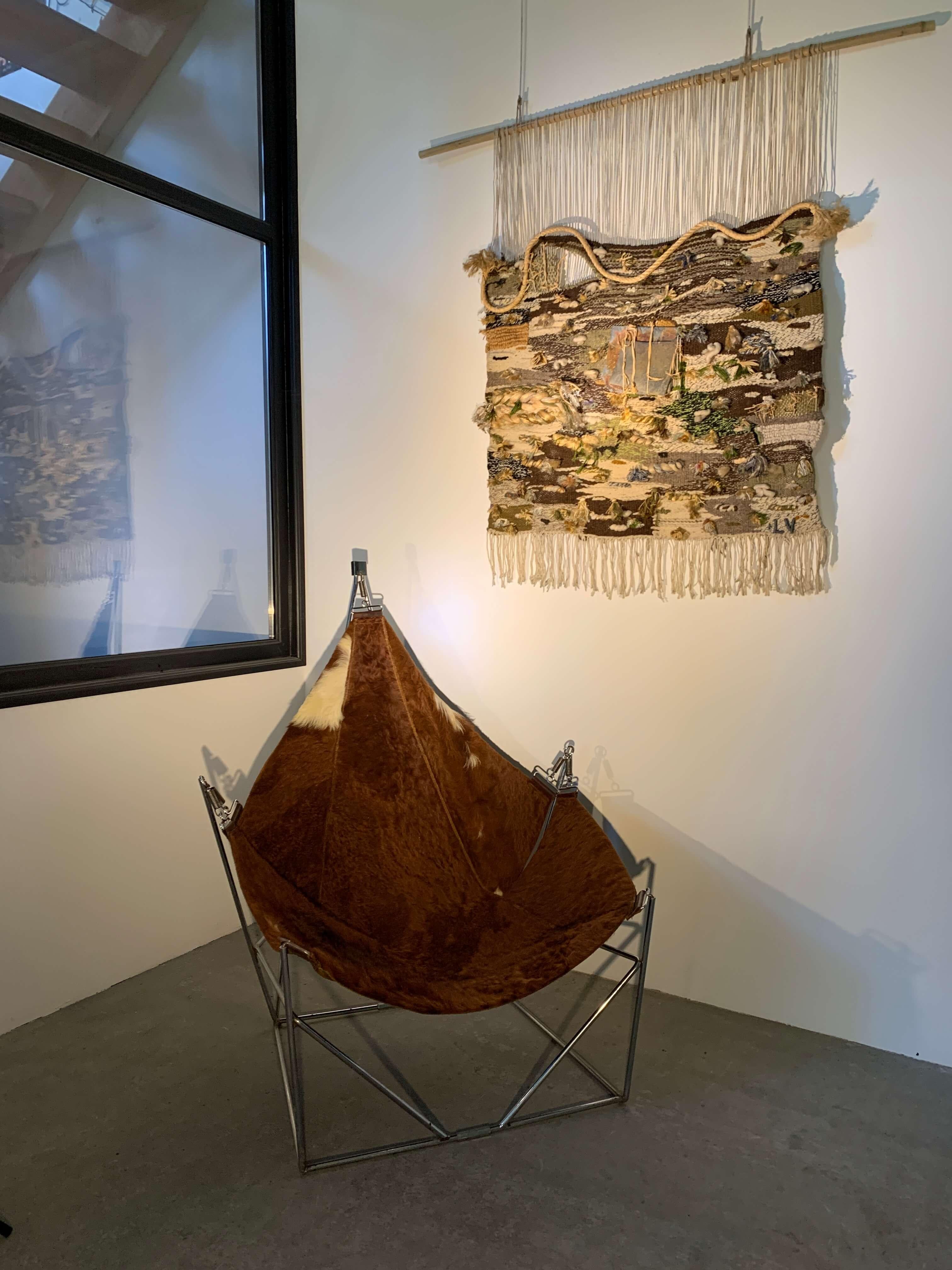 The tapestry evokes a striking brutalism. 
The artist has meticulously woven with a variety of materials : jute, ropes, cotton, wool, intertwining them, twisting them, binding them in a symphony of tangled textures. In the center, two stones mark a