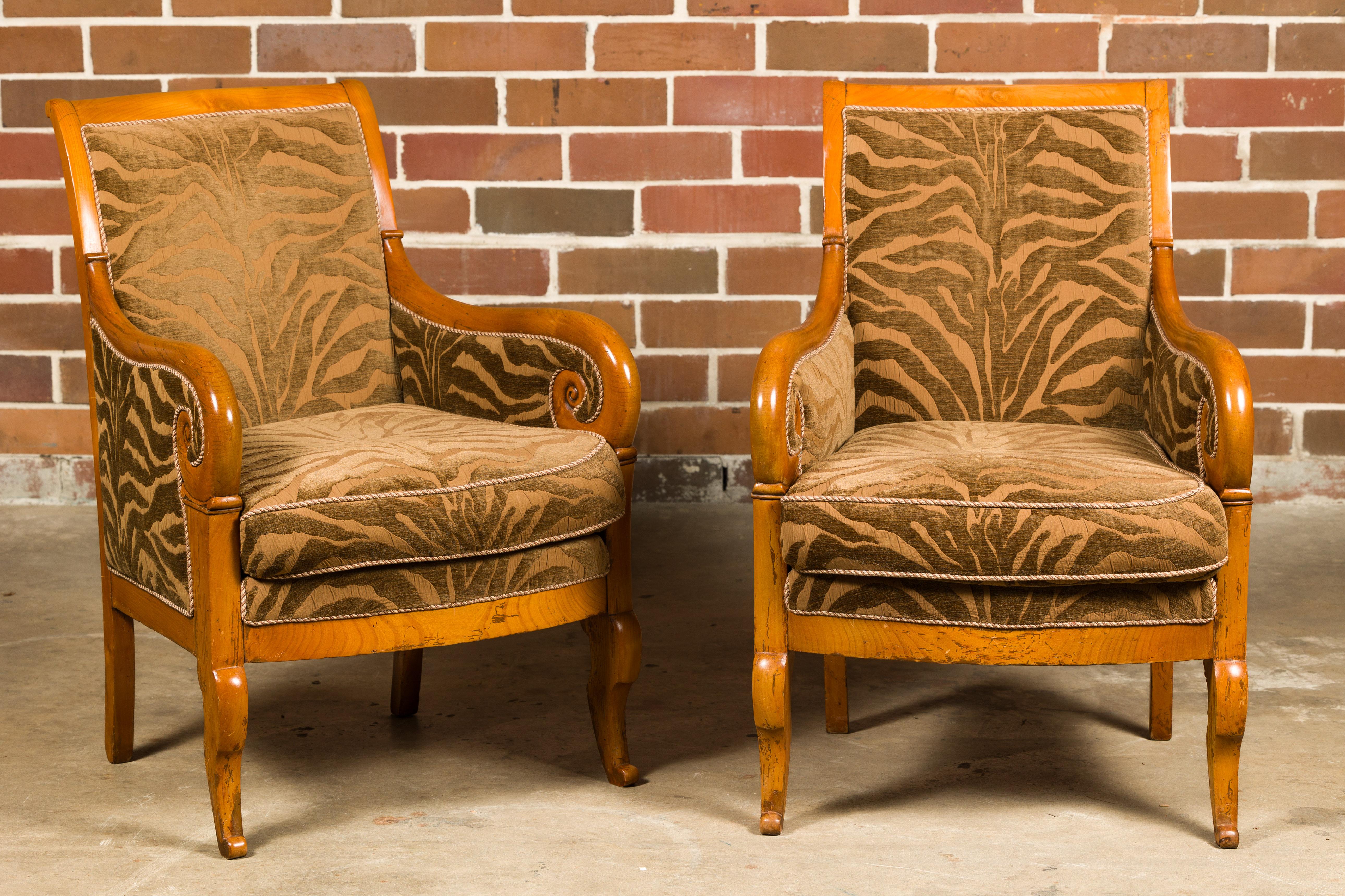 Paire de chaises bergère en noyer de style Louis Philippe du 19e siècle, avec des accoudoirs à volutes, des pieds avant sculptés et une tapisserie d'ameublement zébrée. Cette splendide paire de chaises bergère en noyer de style Louis Philippe,