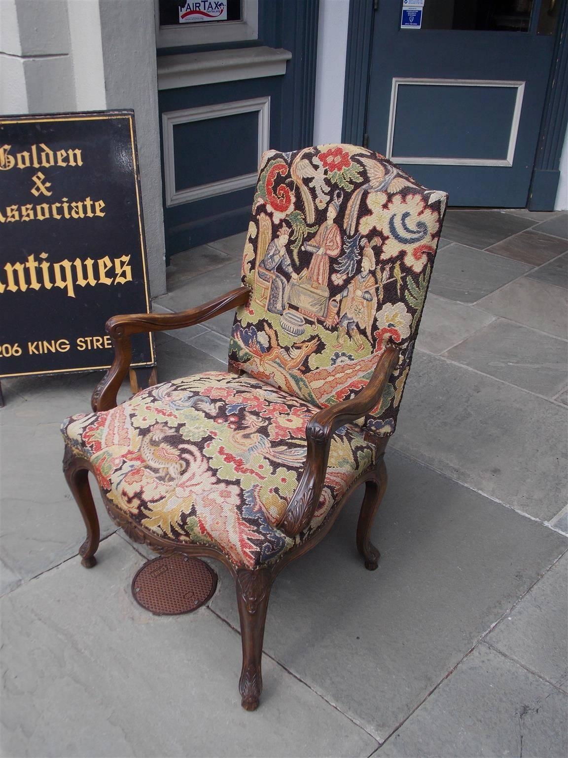 French walnut armchair with a crested upper back, carved scrolled acanthus arms, decorative floral figural needlepoint, centered lower shell carvings, and terminating on the original shell knee carved cabriole legs, Mid-19th century.