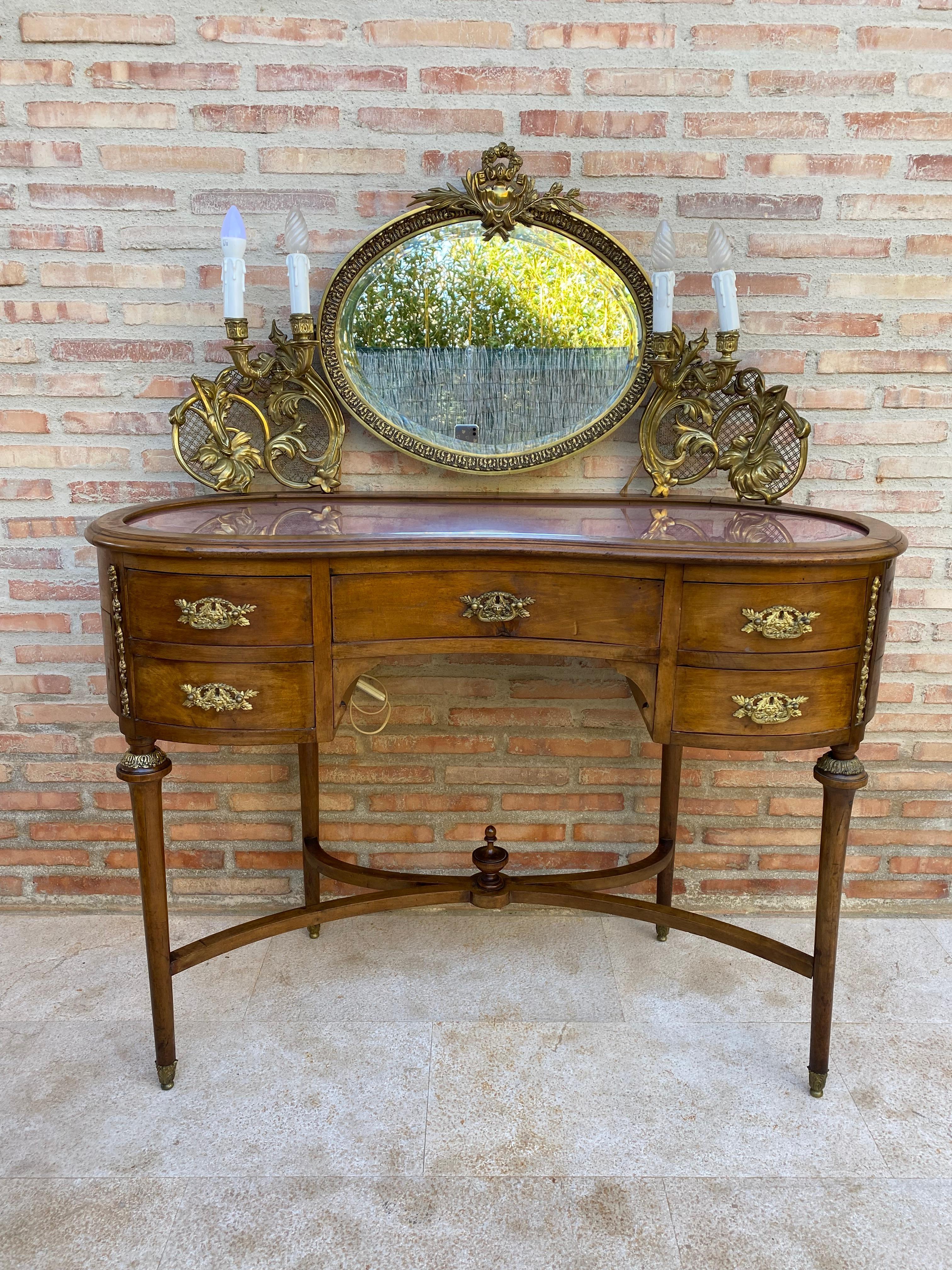 A fine French Louis XVI style dressing table with bronze decorations, having a kidney-shaped top with a gilt bronze frame and a superstructure supporting an oval mirror flanked by gilt bronze scrolled candle arms, above a drawer of central and four