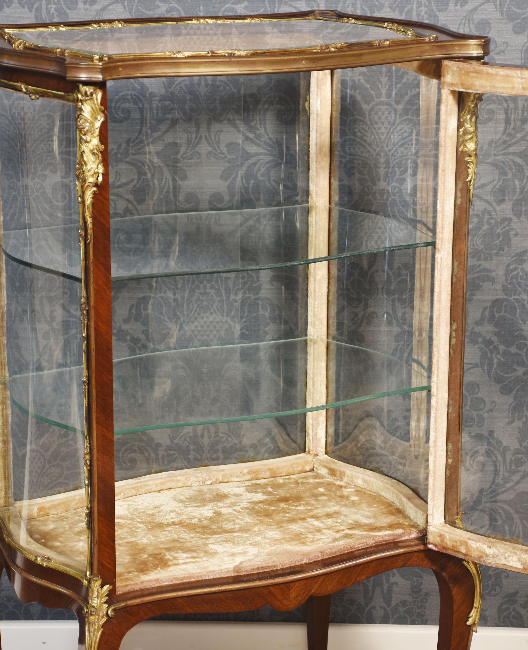 Französischer Nussbaum-Bijouterie-Schrank im Louis-XVI-Design, in Serpentinenform mit vergoldeten Metallbeschlägen verziert. Die abgeschrägte Glasplatte und die geformten, verglasten Seiten führen zu einer großen eintürigen Öffnung, die zwei