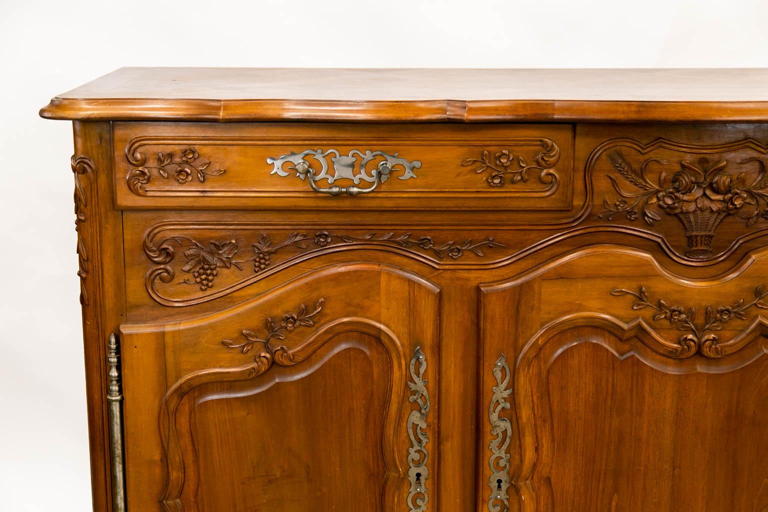 The top of this buffet has an inlaid marquetry center panel with a shaped molded top. The steel fretwork handles, escutcheons, and large barrel escutcheons are original. The front is profusely carved with floral swags, baskets of fruit, and a