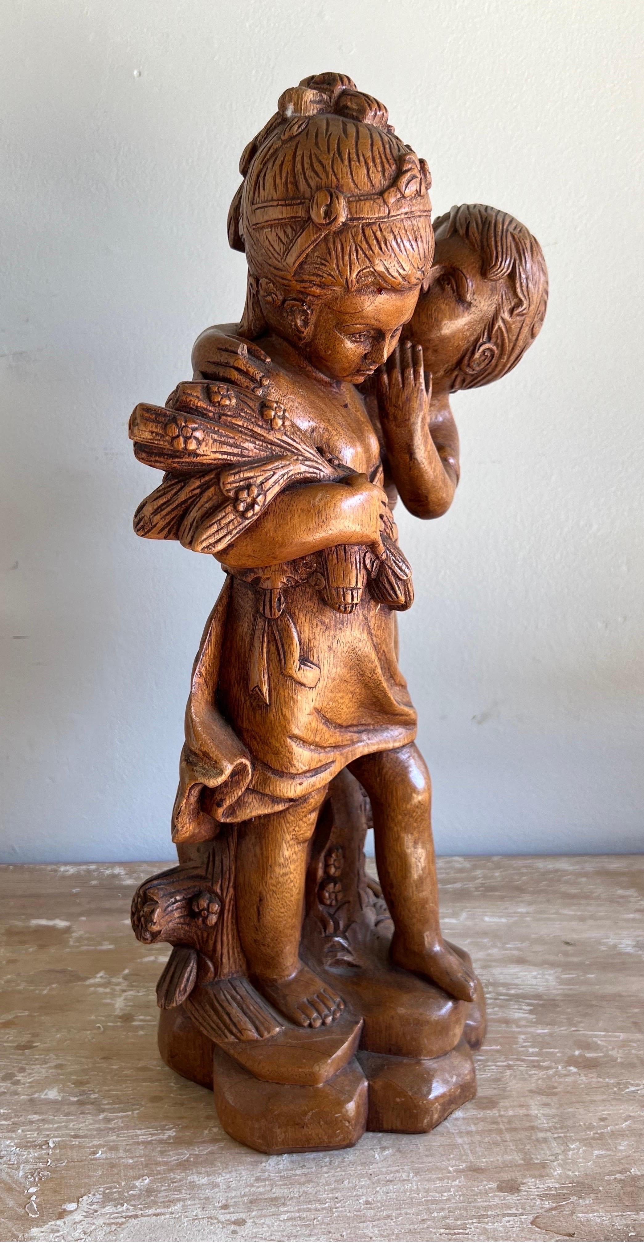 The wood figurative carving of a boy whispering in a girl's ear, with the girl holding a bouquet of flowers in her hand, made from walnut, likely captures a moment of innocence and romance.  The use of walnut adds warmth and a timeless quality to