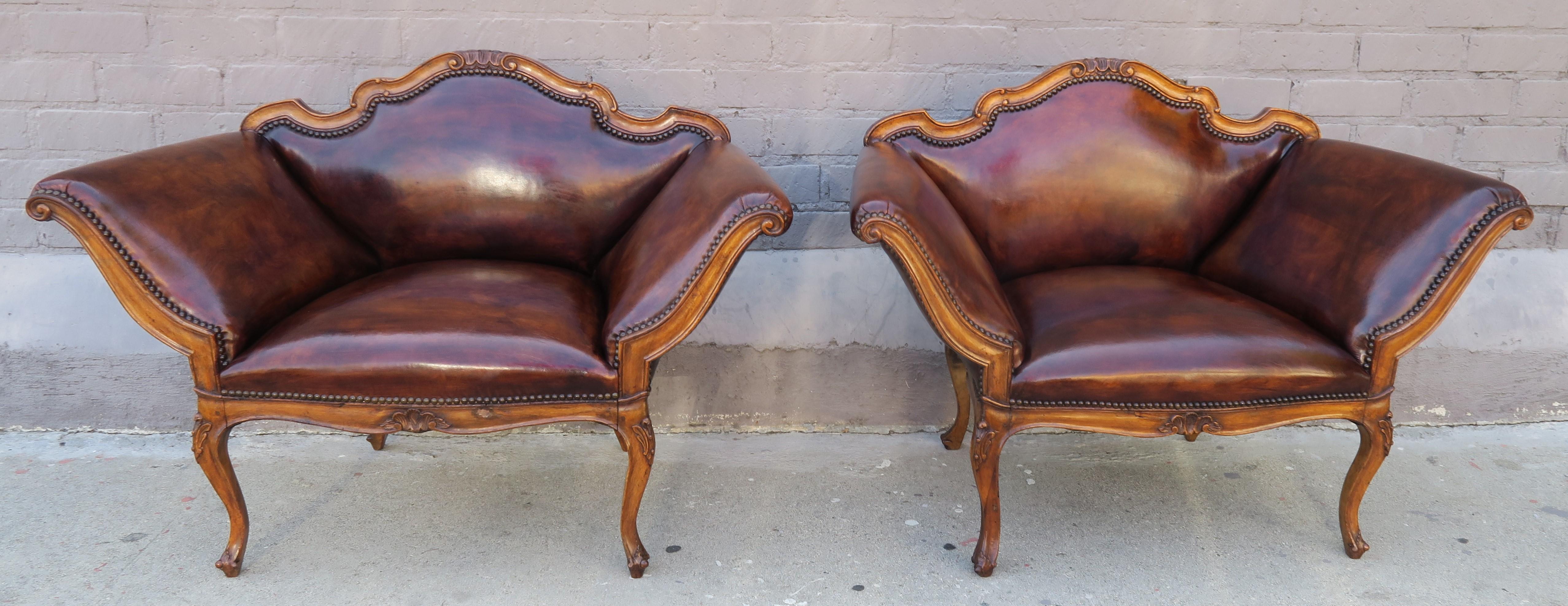 Pair of French carved walnut leather upholstered armchairs with antique brass colored nailhead trim detail. The chairs stand on four cabriole legs. This unique pair of leather armchairs have beautiful lines and would be a great addition to any