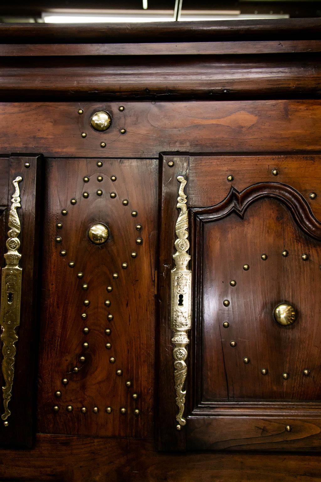 This four door/two drawer cupboard has exposed peg construction throughout. The sides each have five recessed panels. The engraved brass escutcheons and other hardware are original. The top section has a central divider and one fixed shelf in each