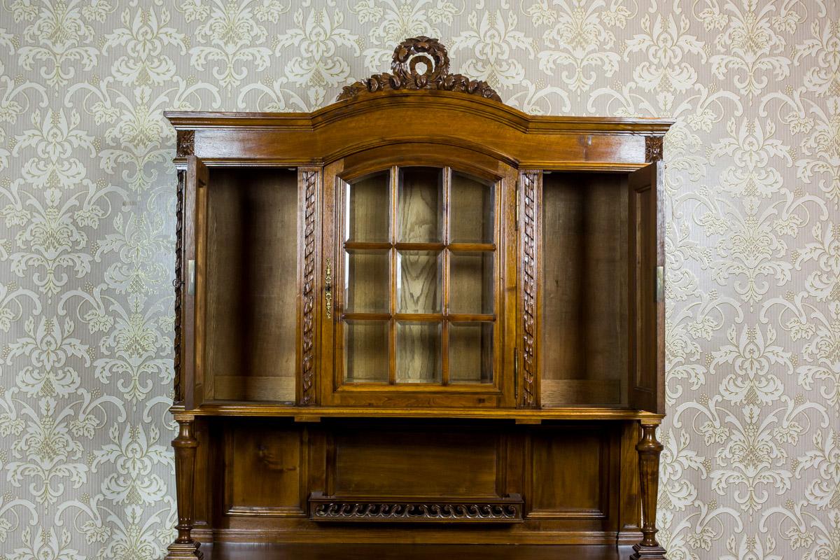 We present you this cupboard, circa the early 20th century, made of walnut wood and partially of softwood covered with walnut veneer.
The piece of furniture is composed of a two-door base and a three-door upper section, which is topped with a
