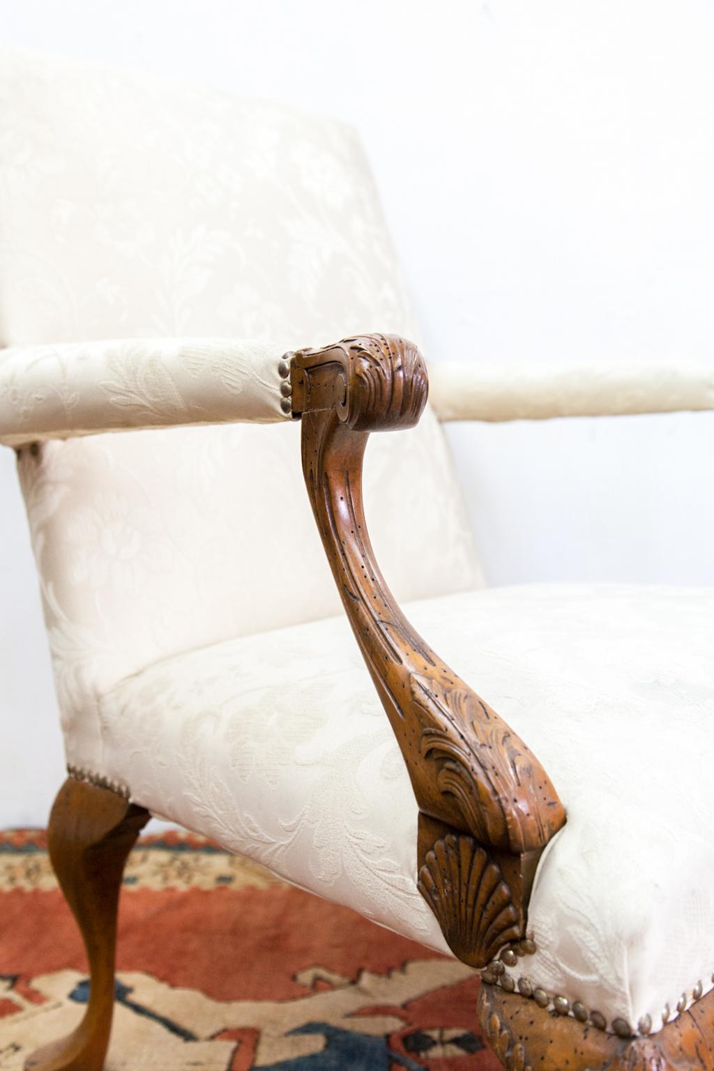 French walnut damask armchair with acanthus carved arms and legs, neatly carved shell motif on the base of each arm. It has small claw and ball feet. The arms and legs have old worm holes.
  