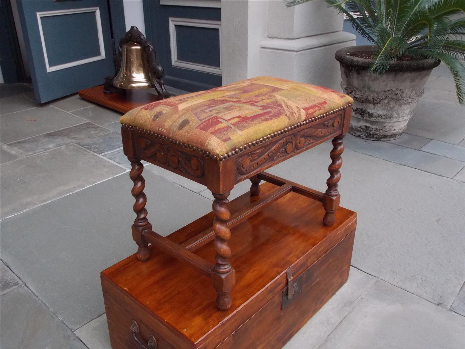 French walnut upholstered stool with brass nail head trim, decorative carved scrolled foliage apron, and resting on the original barley twist legs with connecting stretchers. Mid-19th century.