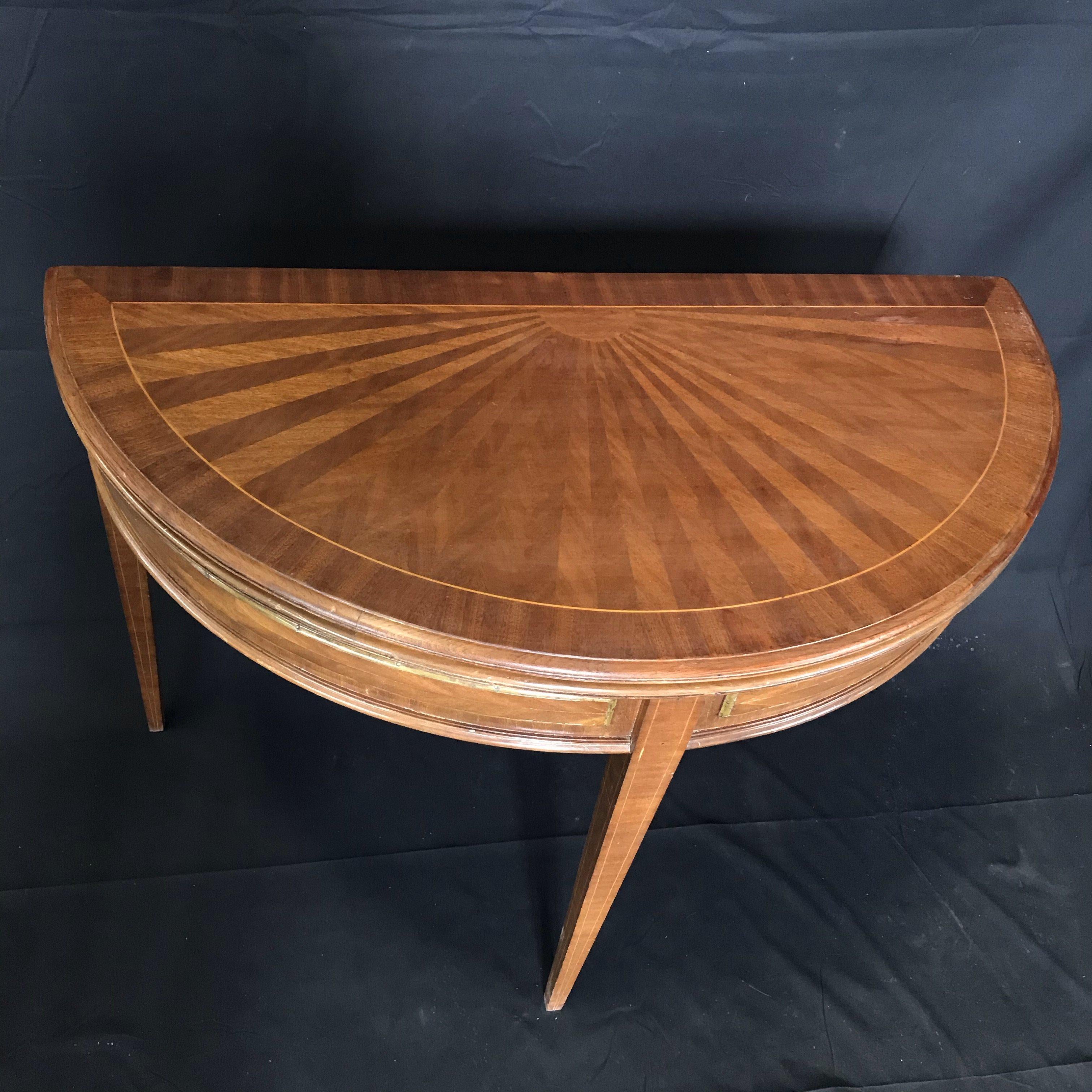 French walnut demilune table or game table when closed 40.75 W 20.75 D. There is a beautiful sunburst pattern inlaid on the top. When open table is round with 40.75 diameter and has an embossed leather interior surface and brass striping on the