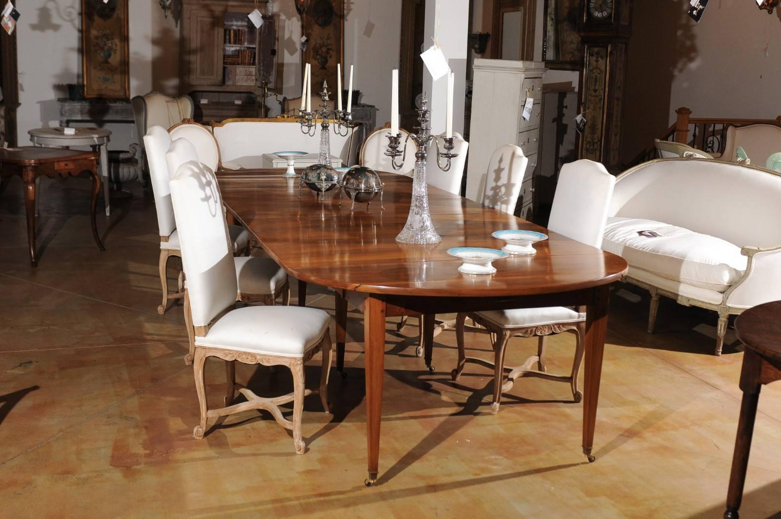 A French walnut extension dining room table with oval top, five leaves, tapered legs and casters from the late 19th century. This exquisite French table features an oval top with small drop leaves on the sides, that extends to become a long dining