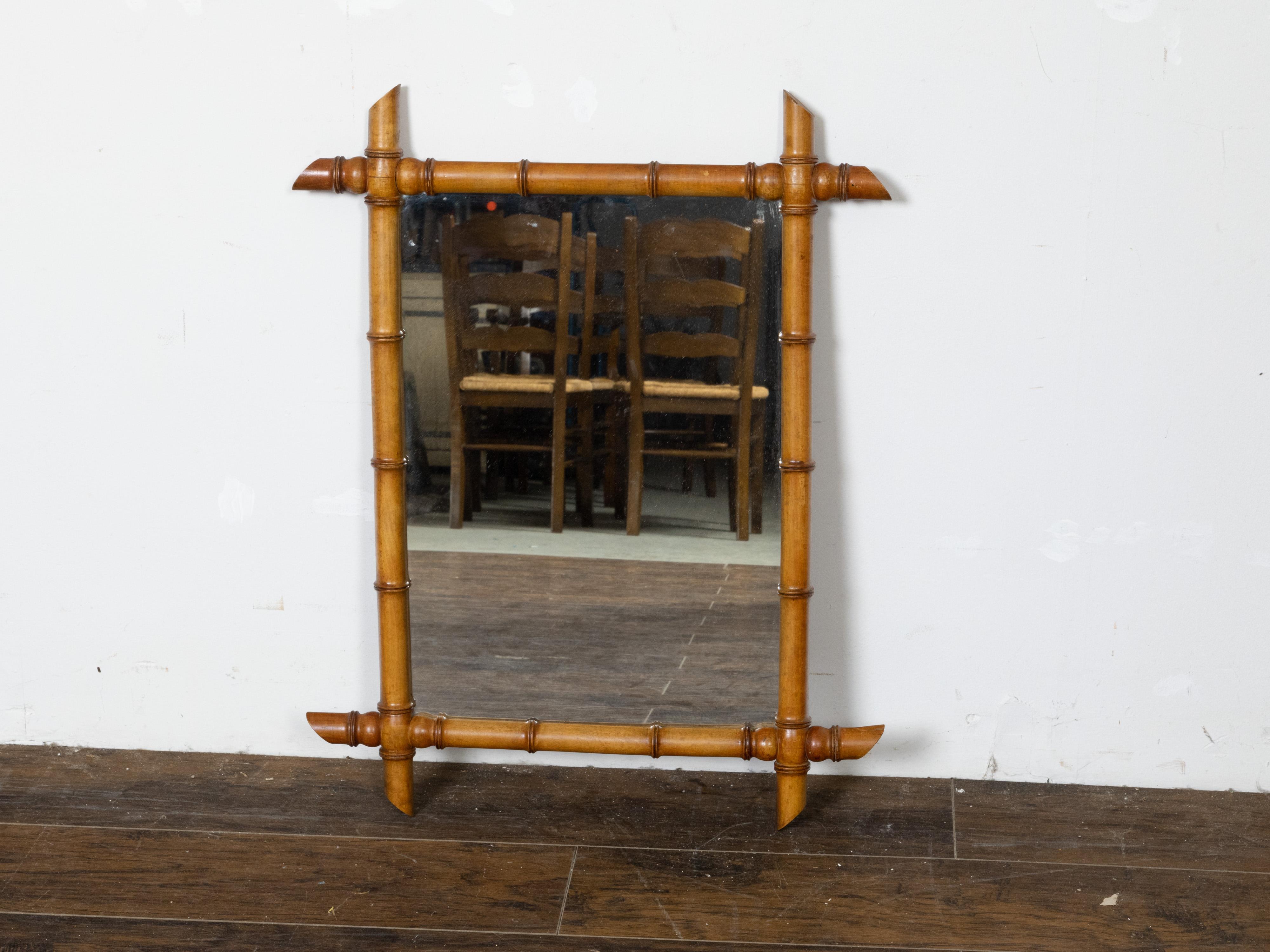 A rustic French rectangular faux-bamboo walnut mirror from the early 20th century, with honey brown patina, intersecting corners and slanted accents. Created in France during the Roaring Twenties in the first quarter of the 20th century, this rustic