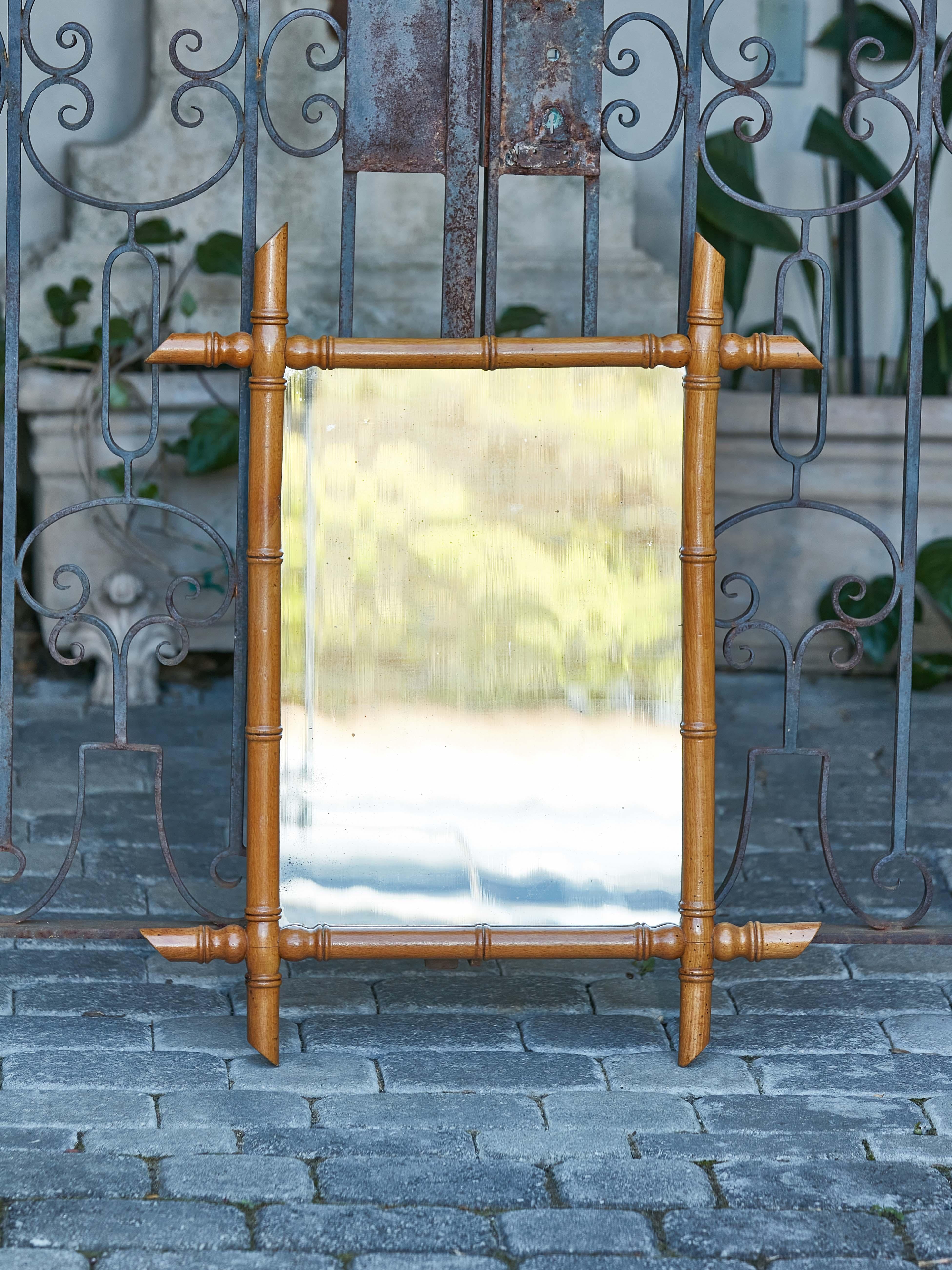 A small rustic French rectangular faux-bamboo walnut mirror from the early 20th century, with light brown patina, intersecting corners and slanted accents. Elevate your rustic decor with this charming small French rectangular faux-bamboo walnut