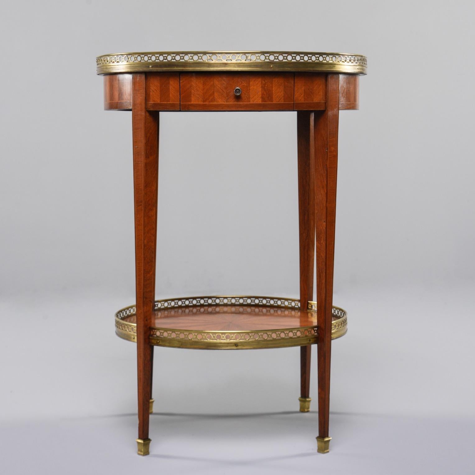 French walnut gueridon with extensive marquetry, circa 1900. Tabletop has checker board pattern, sides have a herringbone pattern and lower tier has a star burst pattern. Single functional drawer, pierced brass gallery on both tiers, and brass foot