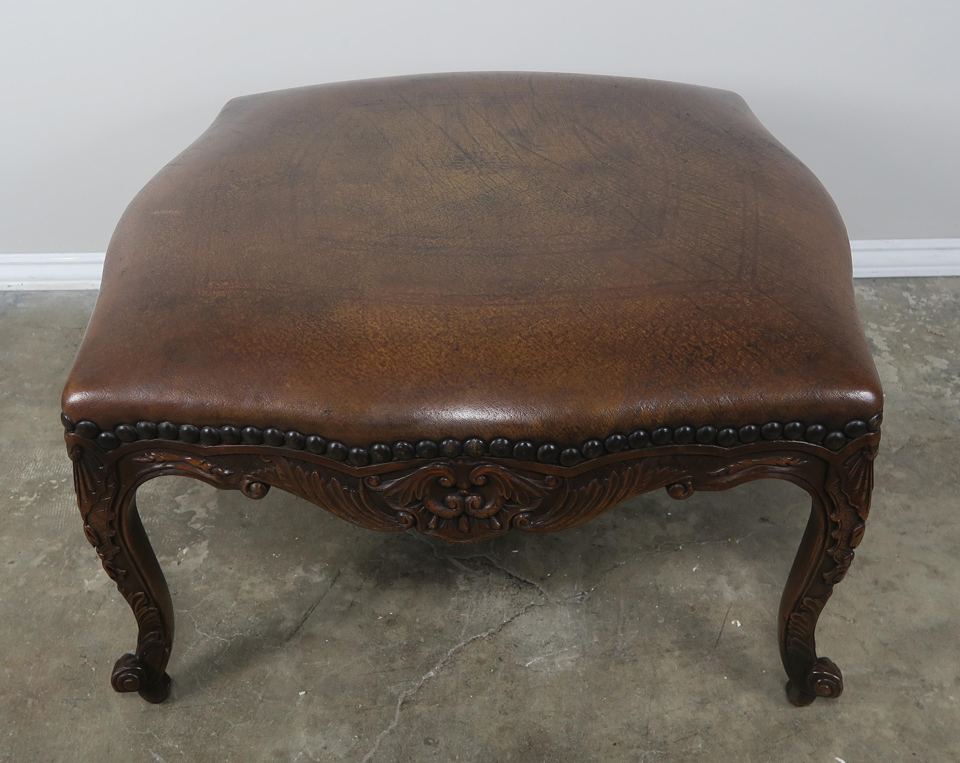 French walnut Louis XV style leather embossed ottoman standing on four cabriole legs that end in ram's head feet. Nailhead trim detail.