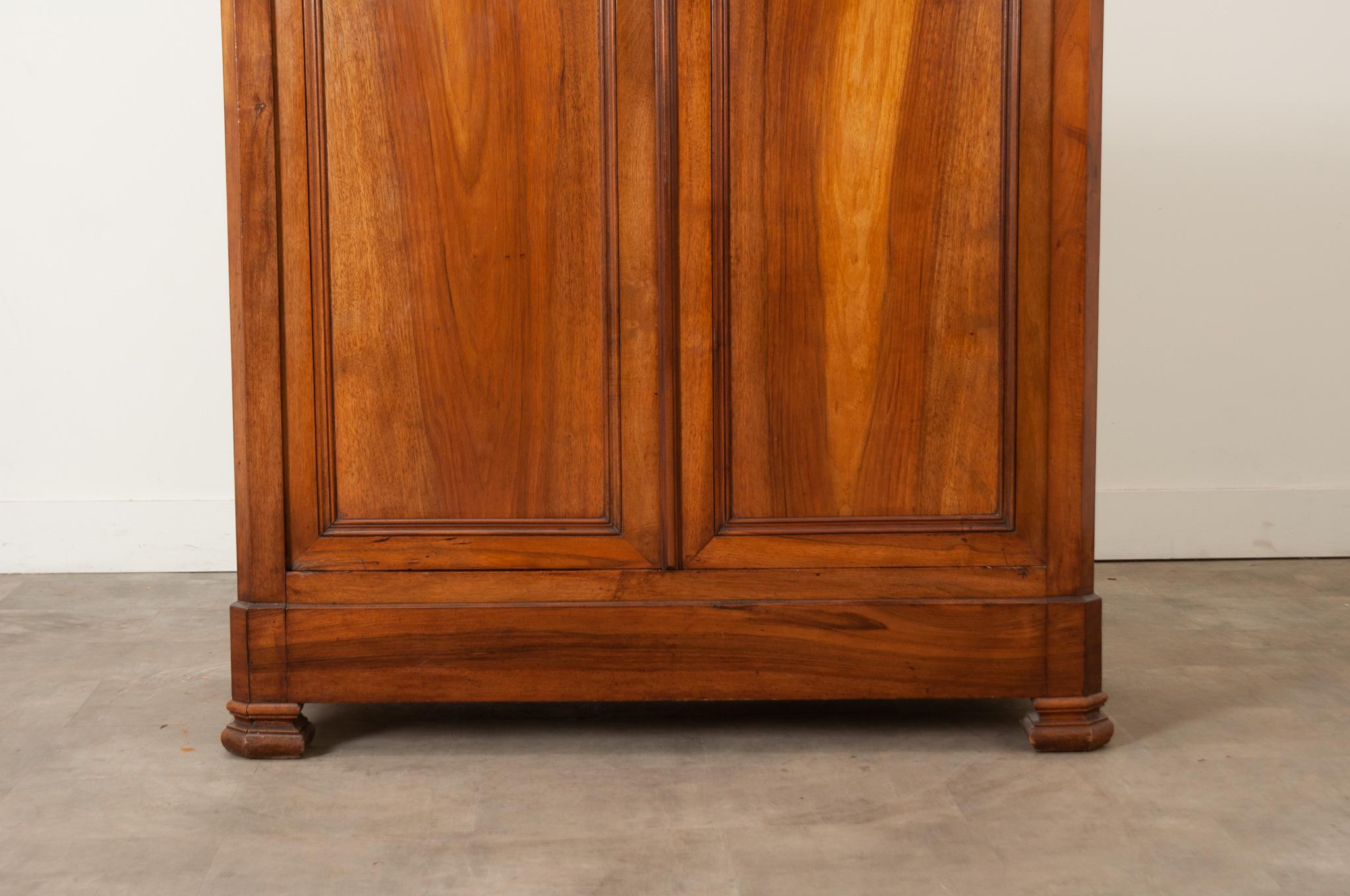 A handsome 19th Century walnut armoire, made in France in the Louis Philippe style. Large paneled doors on hidden hinges are bookmatched. The center lock is functioning and locks with a key. The interior has three fixed shelves, one shelf has two