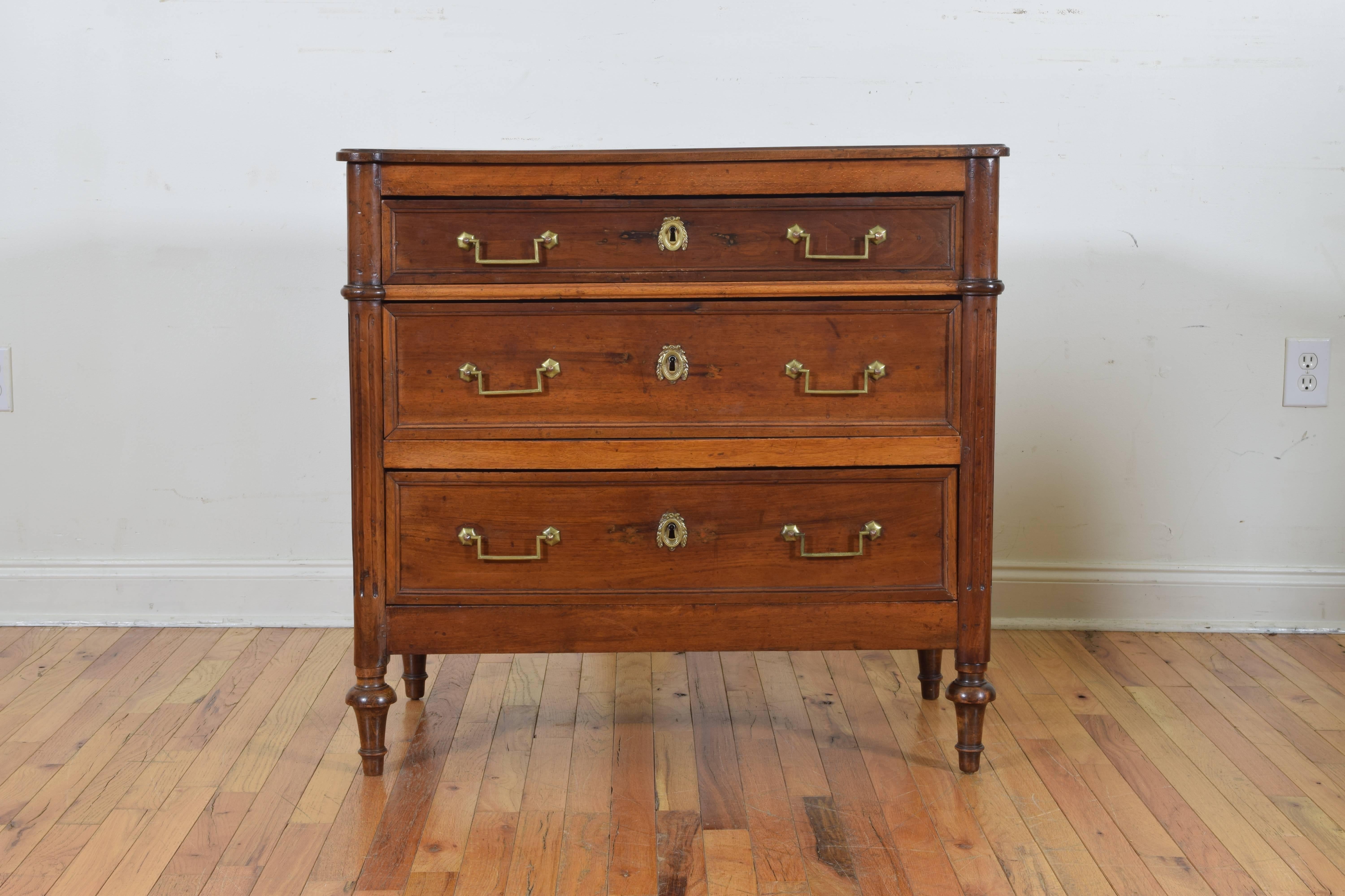The rectangular top with rounded corners atop a conforming case with fluted columnar corners, the three drawers retaining antique handles and escutcheons, raised on shaped and tapering feet.
