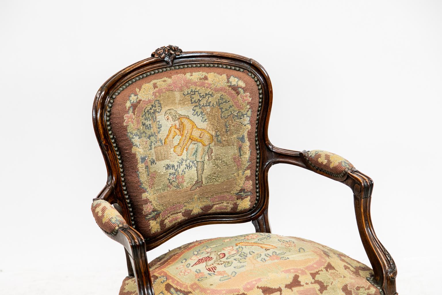 French walnut needlework armchair in the Louis XV style and carved with a floral crest. The needlework seat and back are bordered with brass studs. The man and bird figures in the needlepoint cartouche are done in petit point.
 