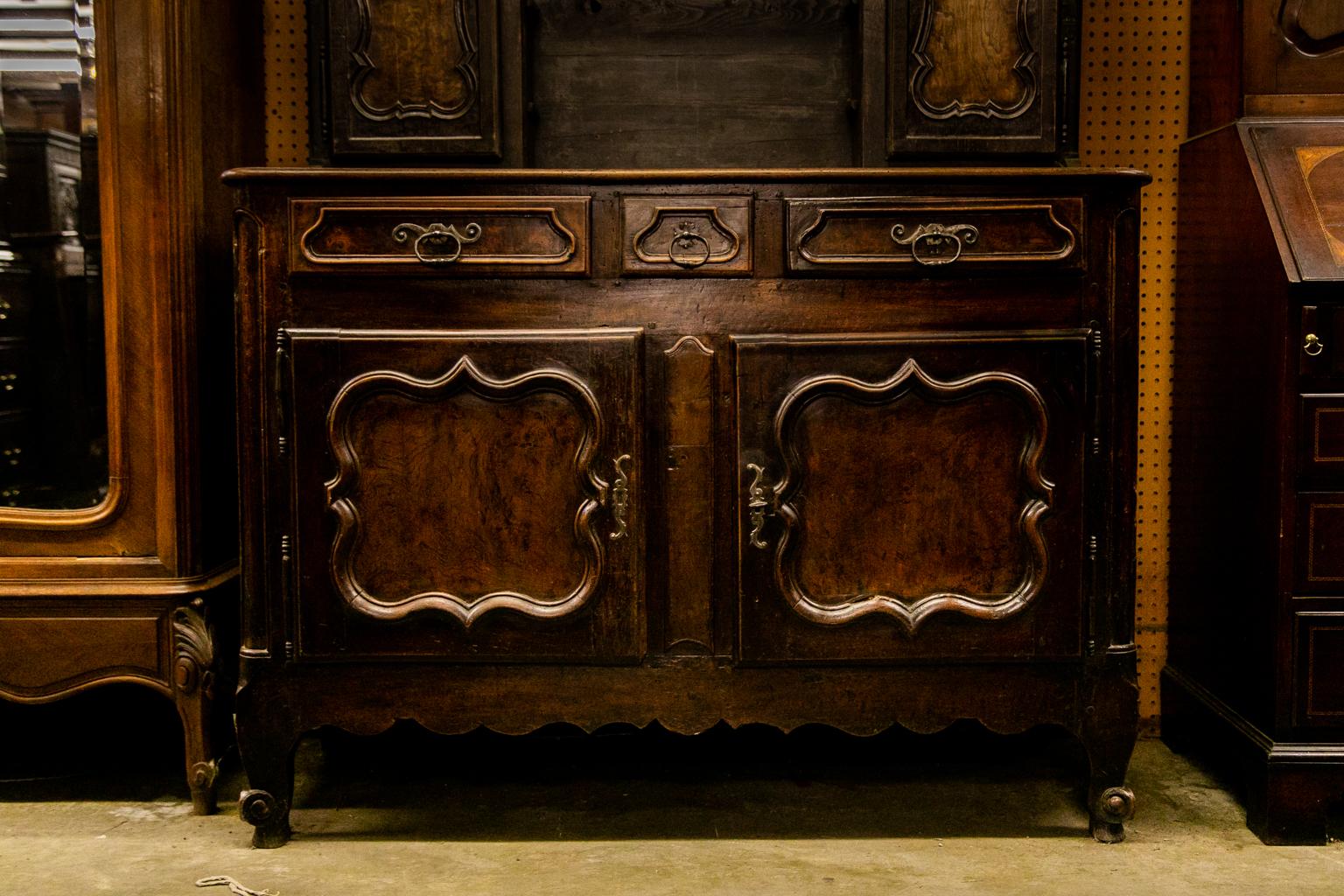 The upper portion of this vassiliere has double pegged construction and has an overhanging cornice with turned pendants. The doors have recessed panels framed with carved scalloped moldings. The lower doors have recessed panels framed with carved