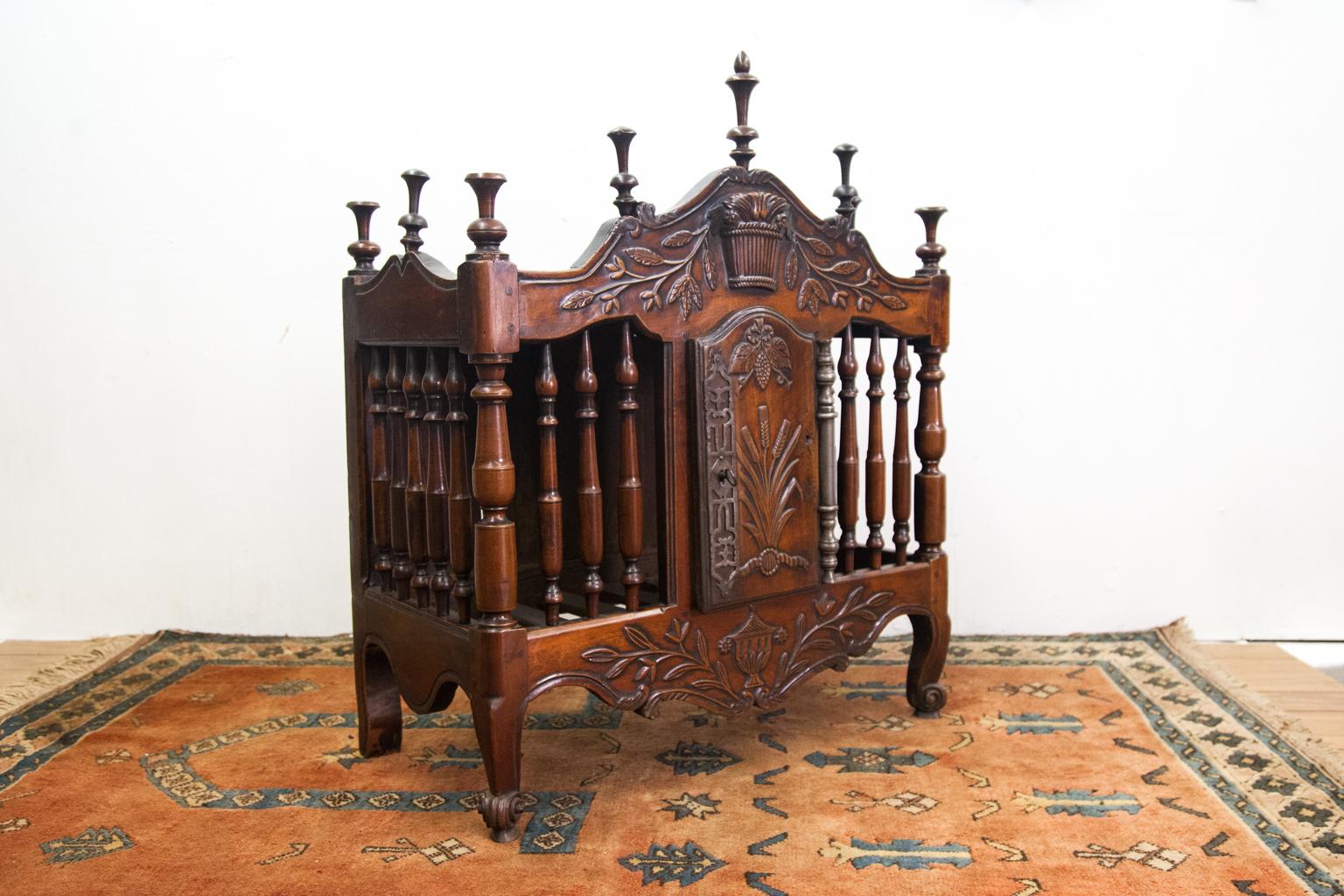French walnut Panetiere with multiple turned finials a top the shaped sides and front, the frieze and apron with carved basket, urn and foliate in relief, front and sides with turned spindles, center door with steel open fretwork escutcheon and