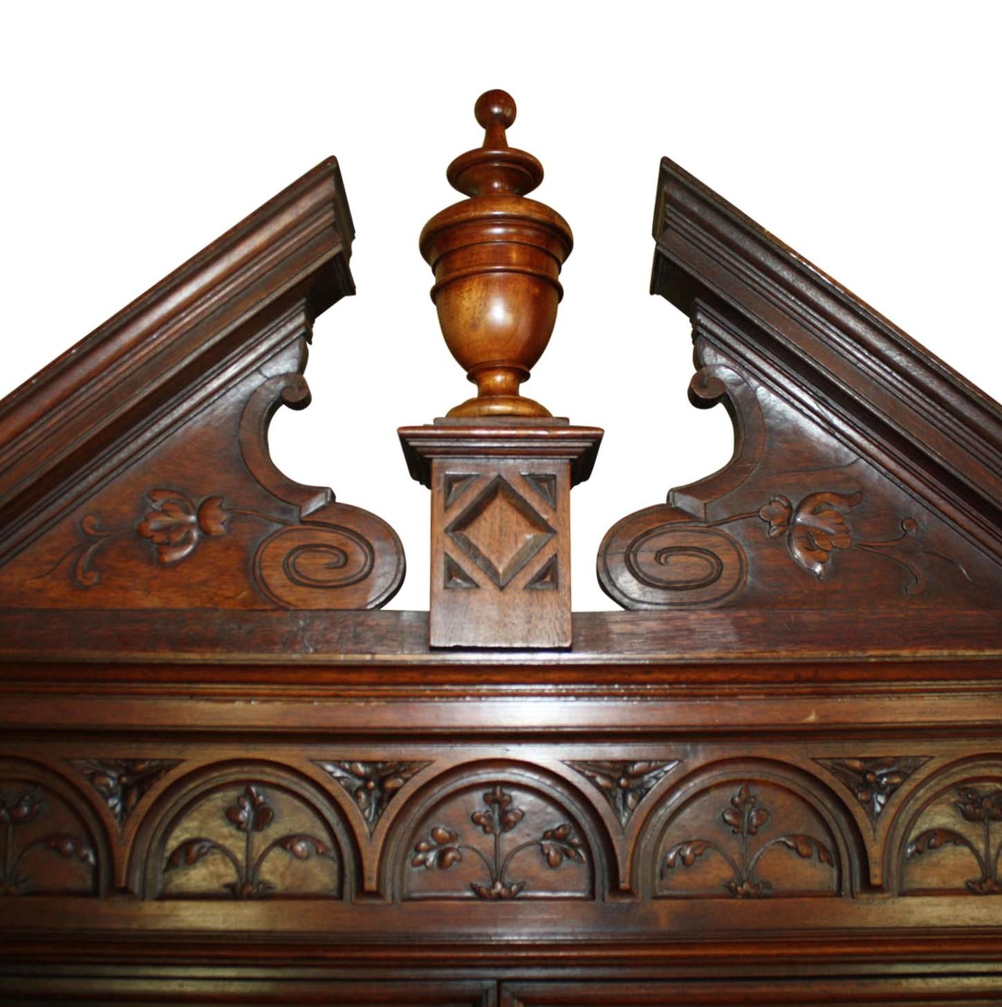Las puertas de cristal emplomado acentuadas con vidrieras azules, rojas y doradas destacan en este precioso armario esquinero. Fabricado en nogal, el mueble presenta tallas en relieve de follaje, flores y crestas que se incorporan con maestría al