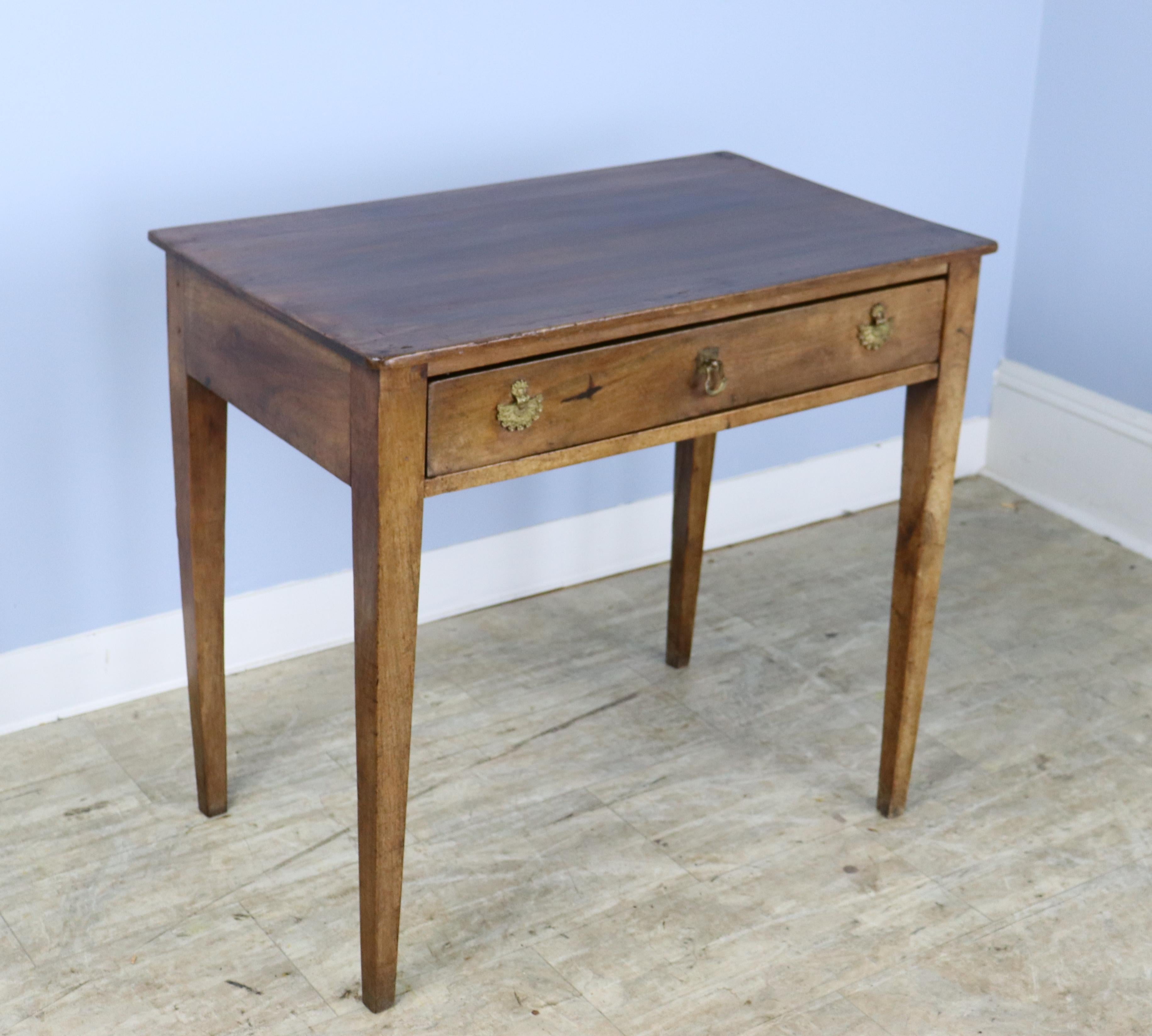 A pretty walnut side table with original pull and ornate brass escutcheons added later. There is a slight warp to the right front leg which does not affect the stability of the piece. No wobbles! Useful divided space inside the single drawer.