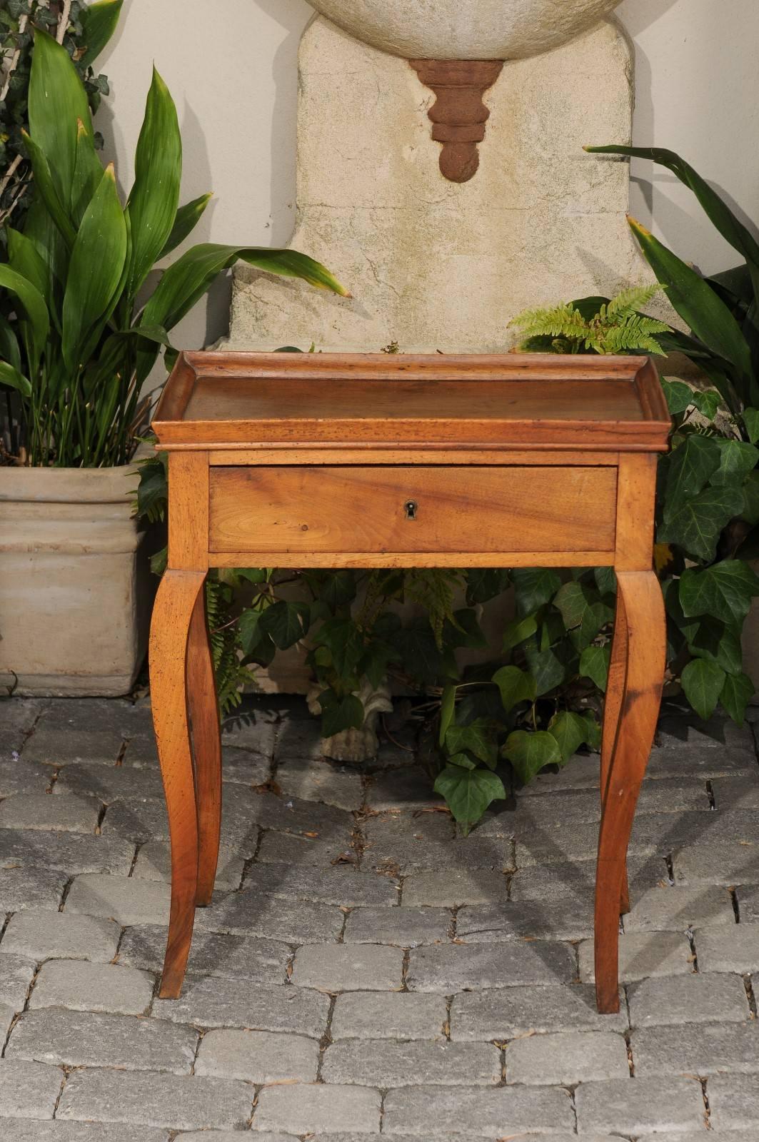 A French walnut side table with tray top and cabriole legs from the mid-19th century. This French side table features a rectangular tray top with slightly concave lines on the longer sides, sitting above a single drawer. The piece is elegantly