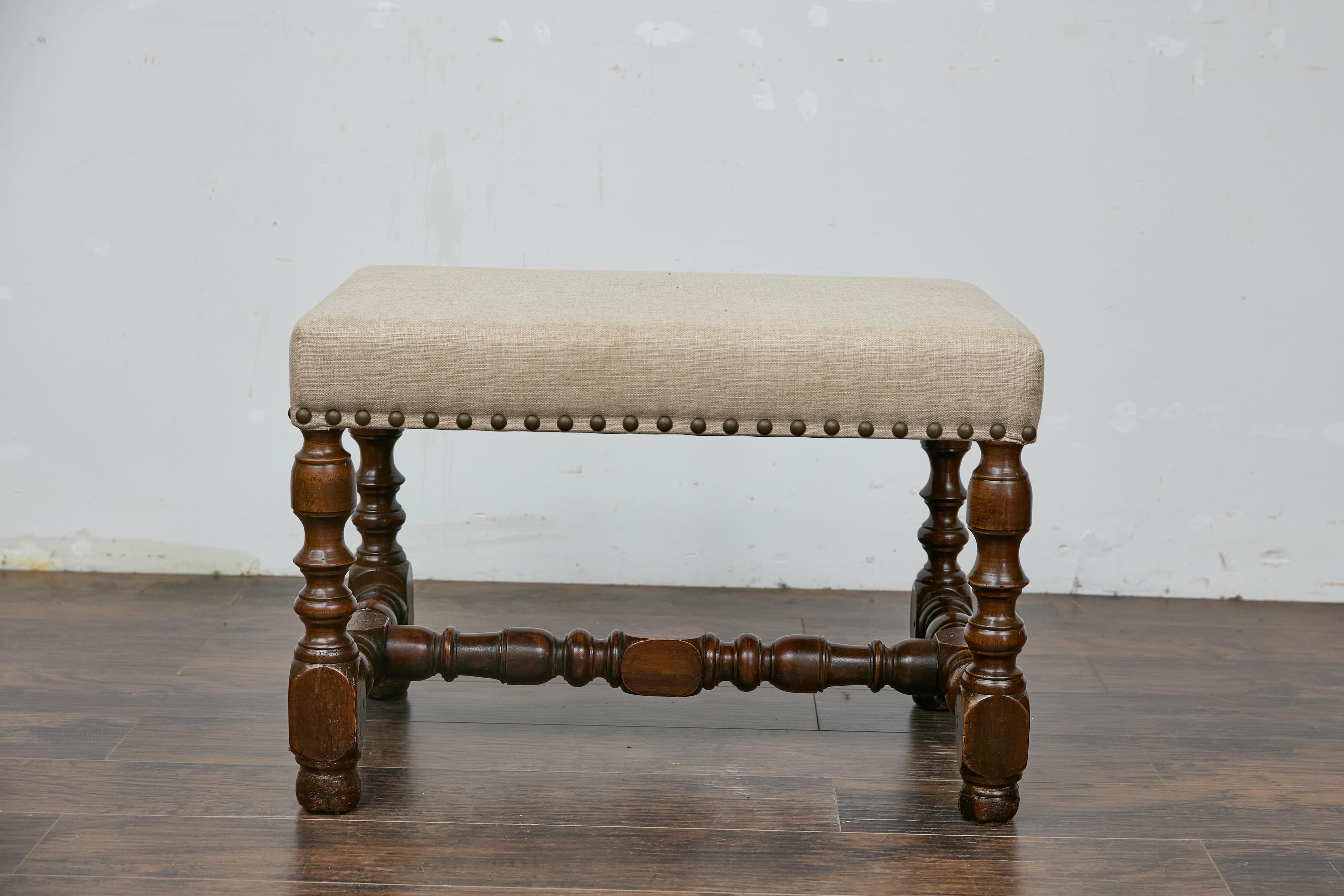 A French walnut stool from the late 19th, early 20th century with turned legs, H-Form cross stretcher and linen upholstery. This French walnut stool from the late 19th to early 20th century showcases elegant craftsmanship with its turned legs and