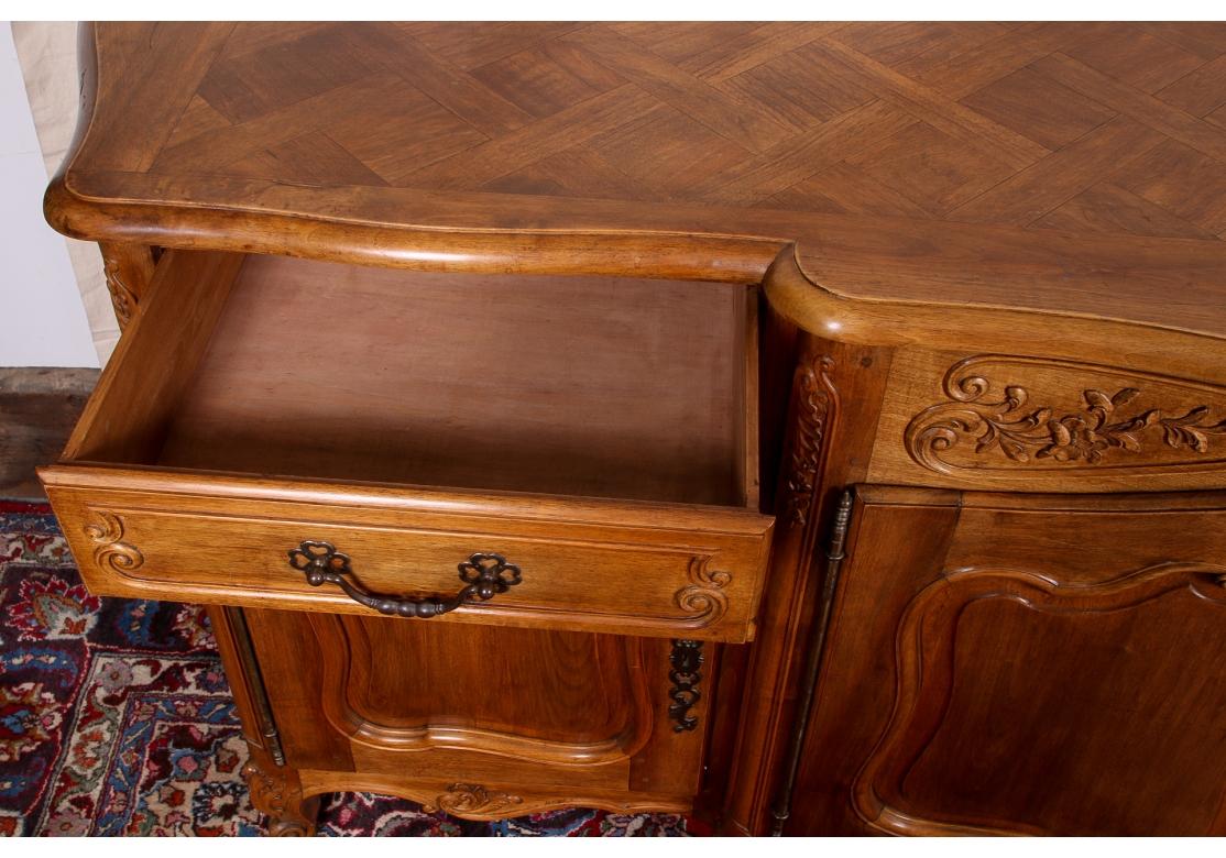 Un mobile in stile francese di grandi dimensioni e di ottima fattura, dalla forma e dalla funzione raffinate. Con un'elaborata cassa sagomata intagliata con decorazioni a volute, lati incassati con porte e scuretti e un armadietto centrale a doppia