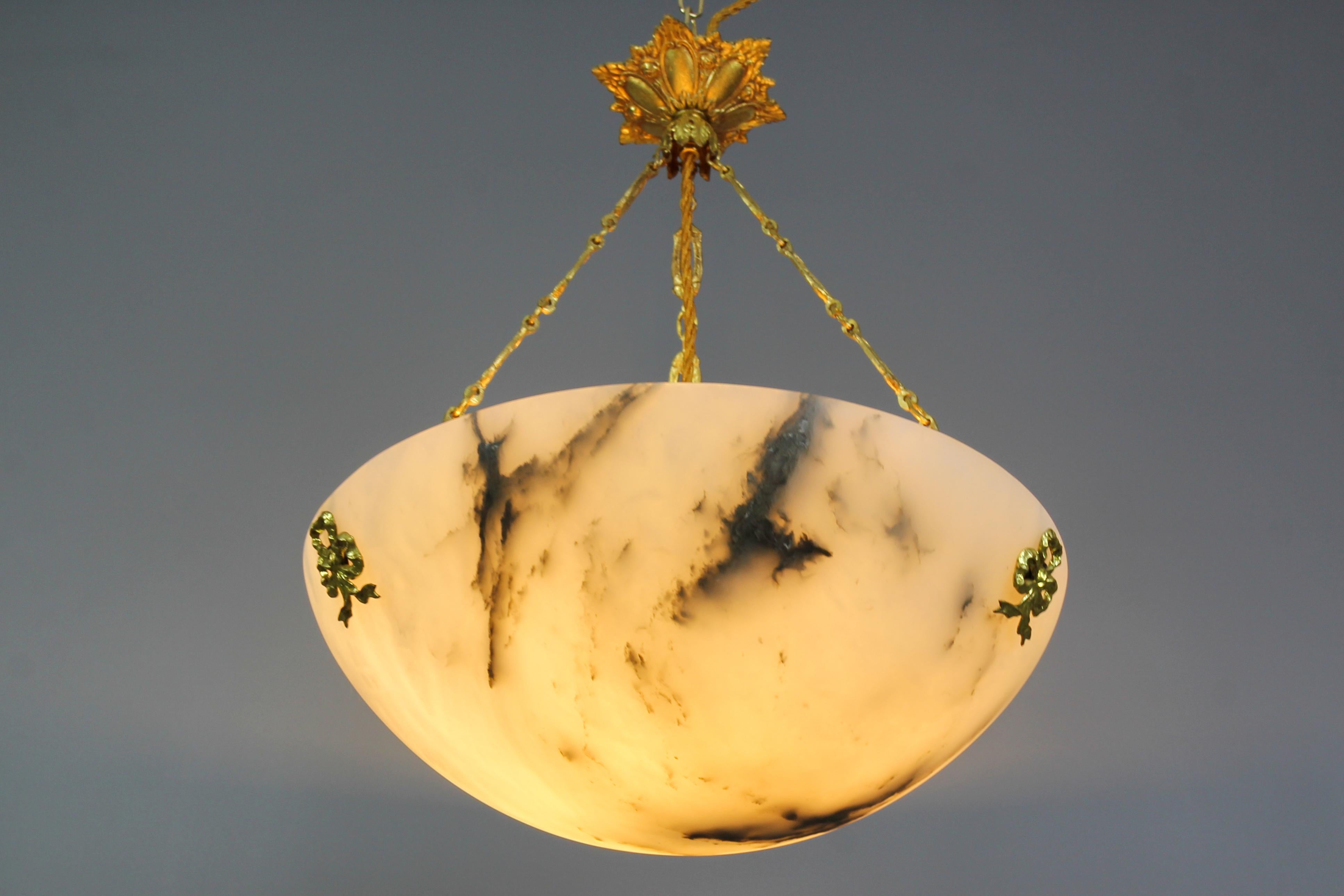 A refined Art Deco white alabaster pendant ceiling light fixture with dark brown and black veins. France, 1920s. This masterfully carved and beautifully veined one-piece alabaster bowl is suspended by three ornate bronze and brass chains and a