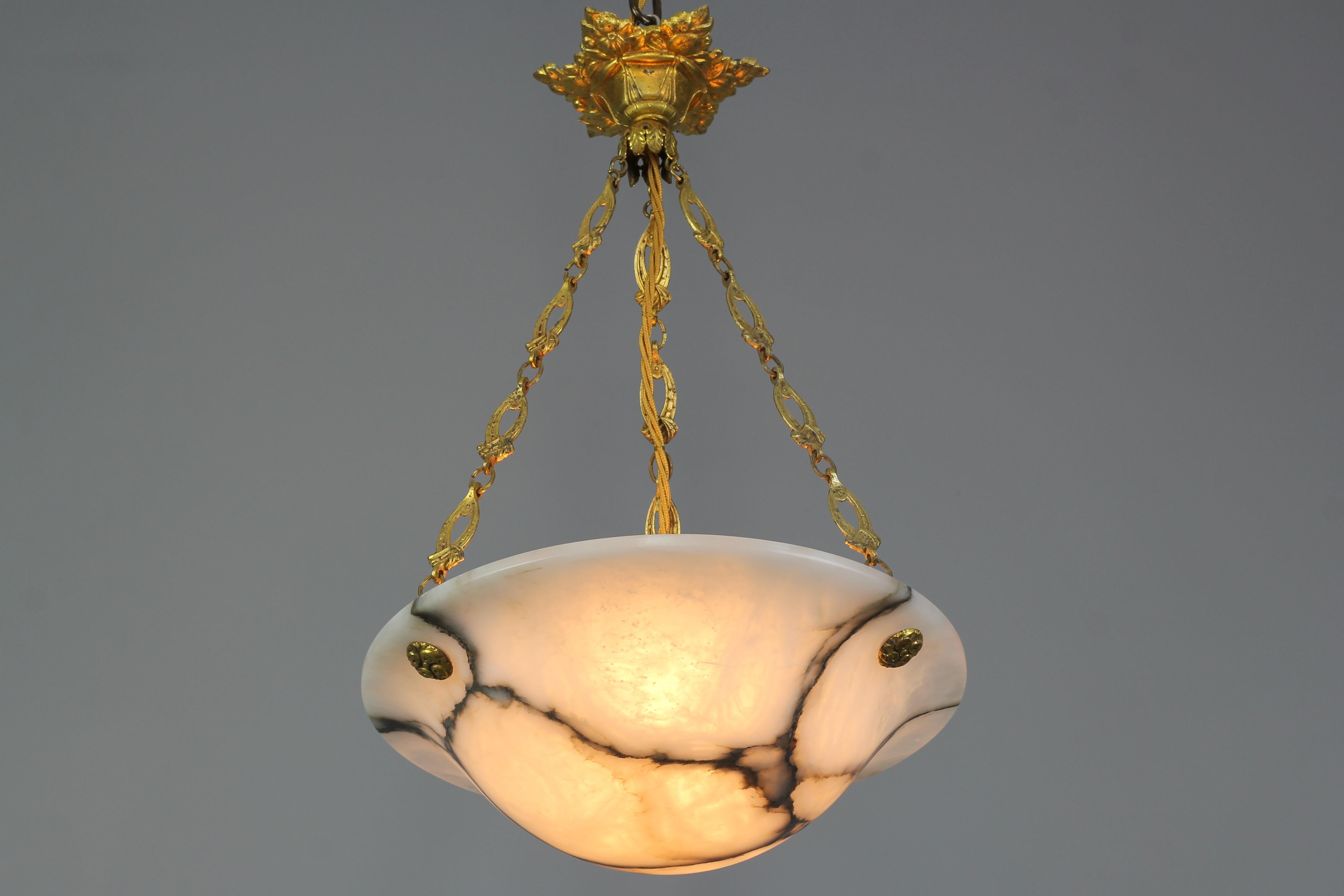 A refined Art Deco white alabaster pendant ceiling light fixture with dark brown and black veins. France, 1930s. This masterfully carved and beautifully veined one-piece alabaster bowl is suspended by three ornate bronze chains and a richly