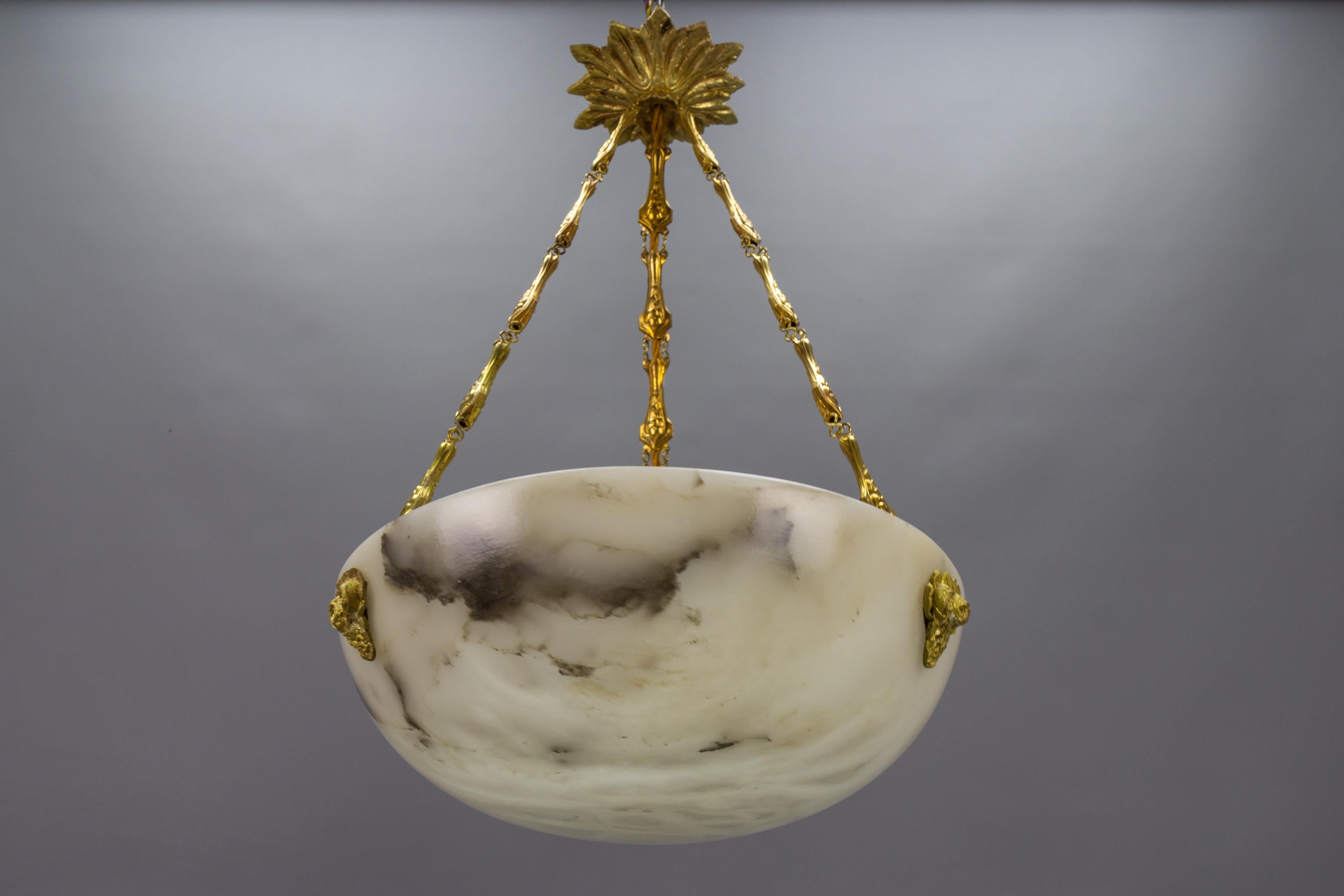 An Art Nouveau period white and black veined alabaster pendant light with bronze and brass fixtures.
An adorable and good-sized alabaster pendant ceiling light fixture from circa the 1920s. Beautifully veined white alabaster bowl suspended by three
