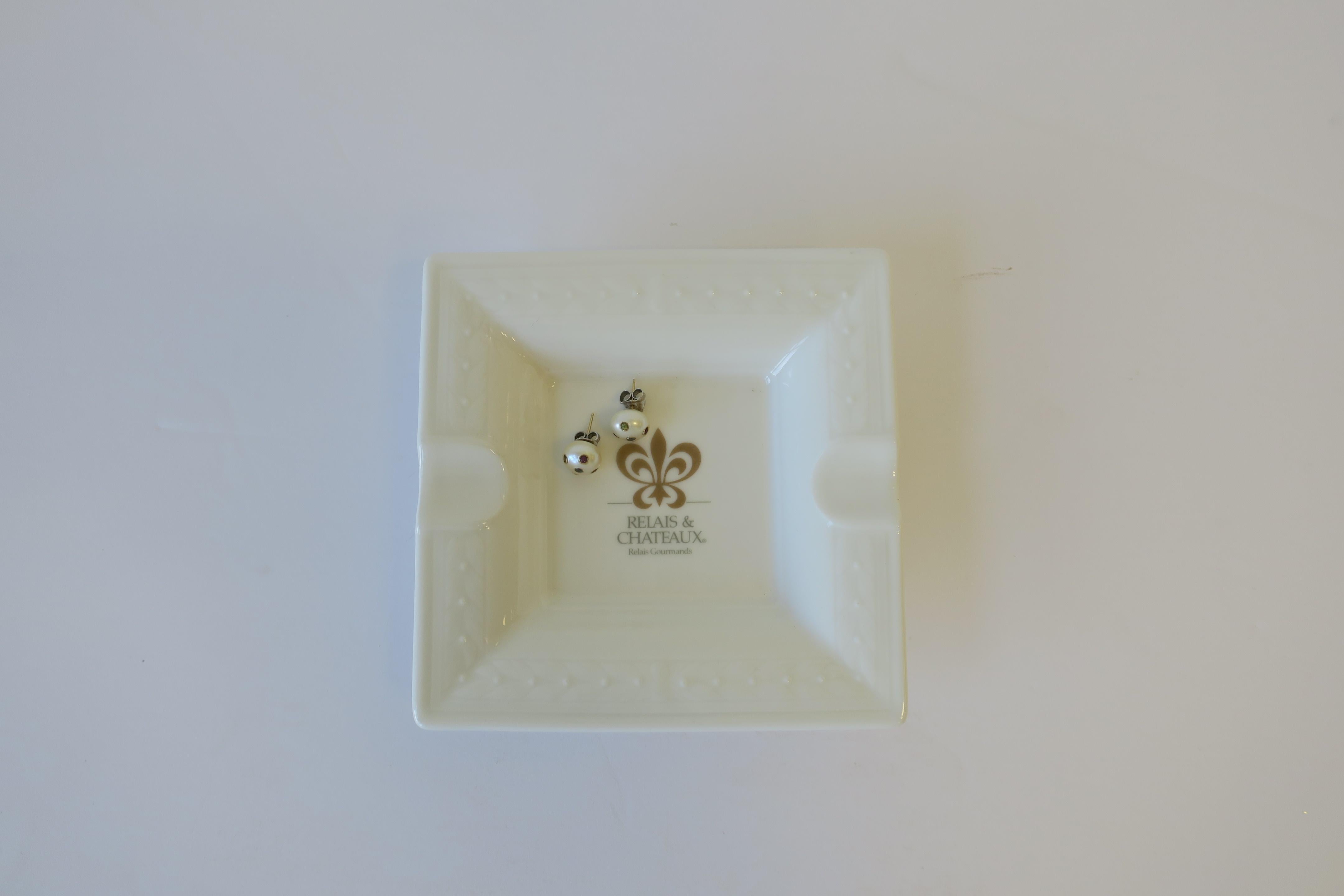 A small square white and gold porcelain dish or ashtray from French luxury hotel brand Chateau & Relias with a beautiful decorative gold fleur-de-lis. With maker's mark on back as shown in image #2. Made by Villroy & Bach, Luxemburg. This small dish